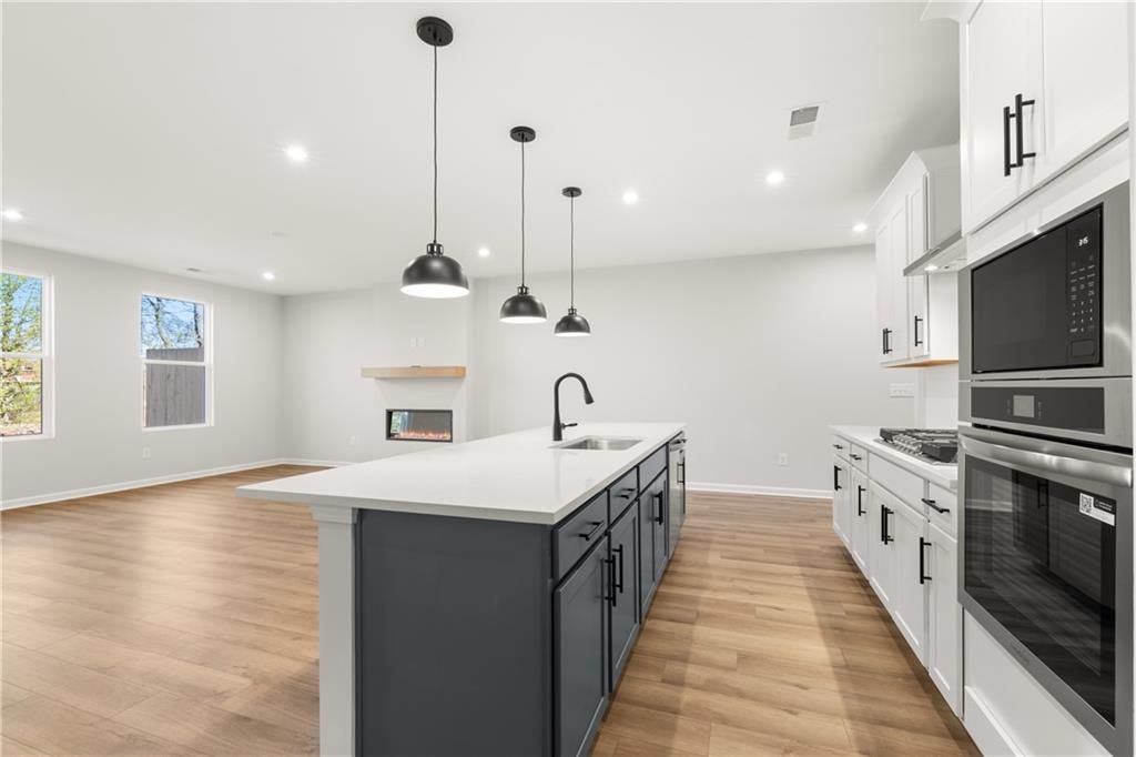 Modern open-concept kitchen with white quartz island, stainless appliances, pendant lights, and adjacent gas fireplace in Davidson Homes The Cary A, Winder, GA