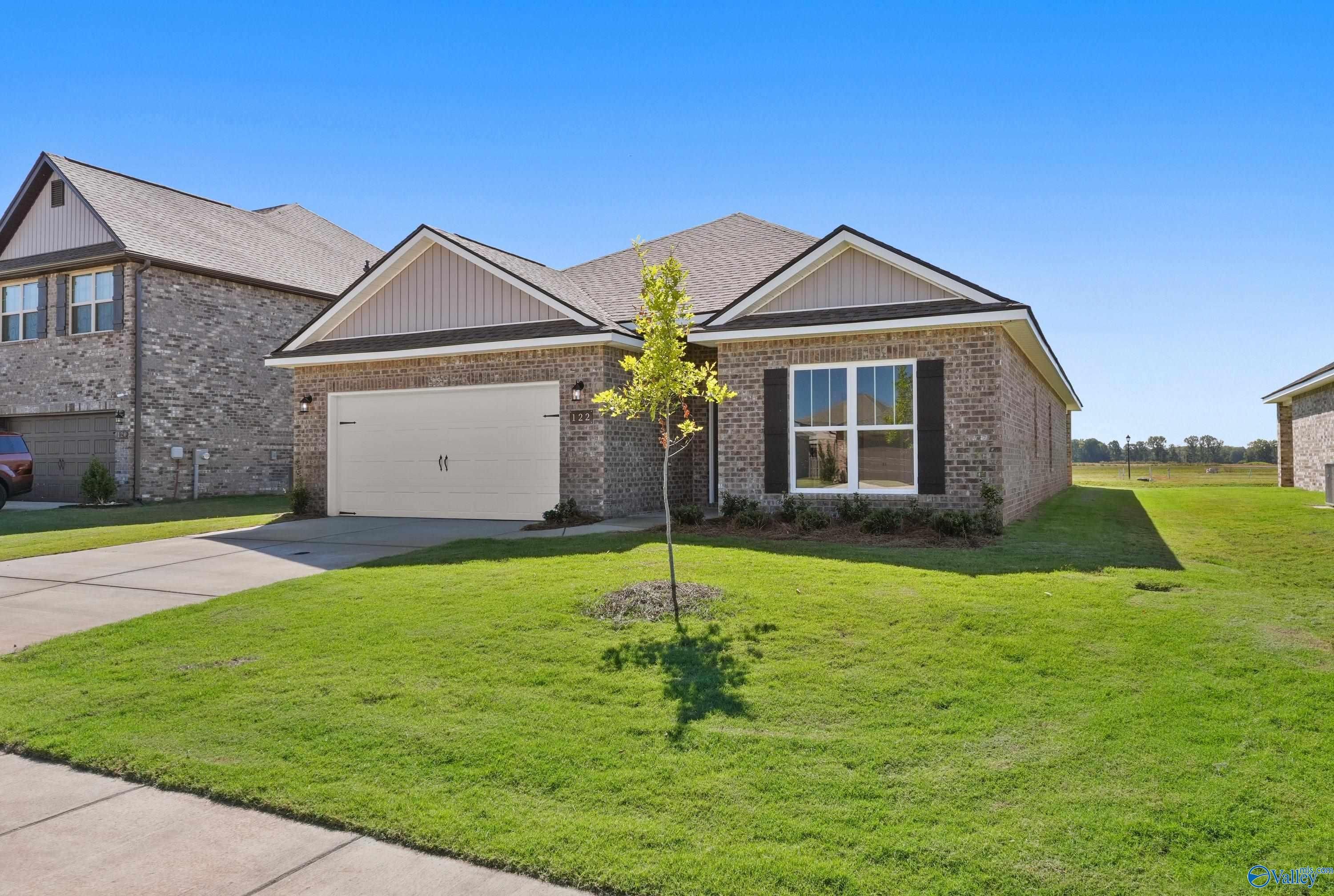 Modern 1-story 4-bedroom home exterior with 2-car garage, brick accents, and young tree in lush front yard, Clearview, Hazel Green, AL