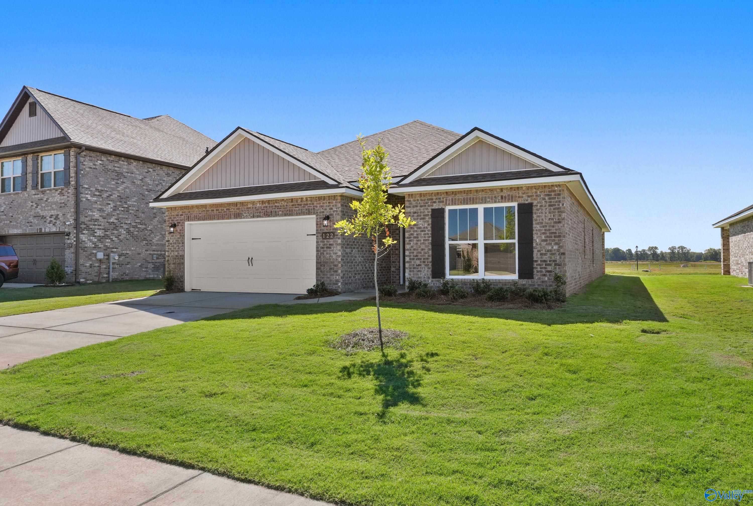 Modern 1-story 4-bedroom home exterior with 2-car garage, brick accents, and young tree in lush front yard, Clearview, Hazel Green, AL