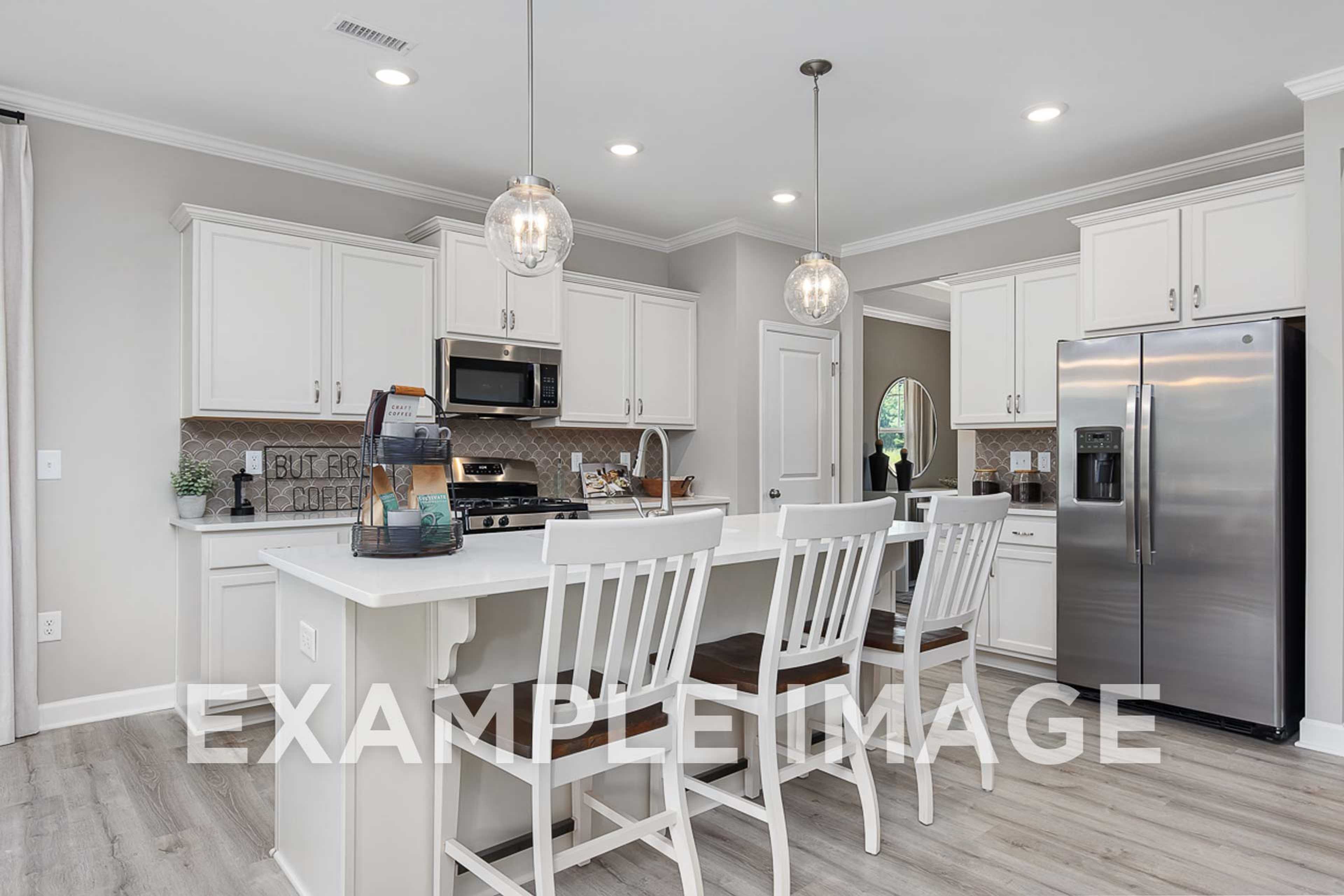 Spacious kitchen in The Ash D home with white shaker cabinets, large center island, stainless steel fridge, and pendant lighting