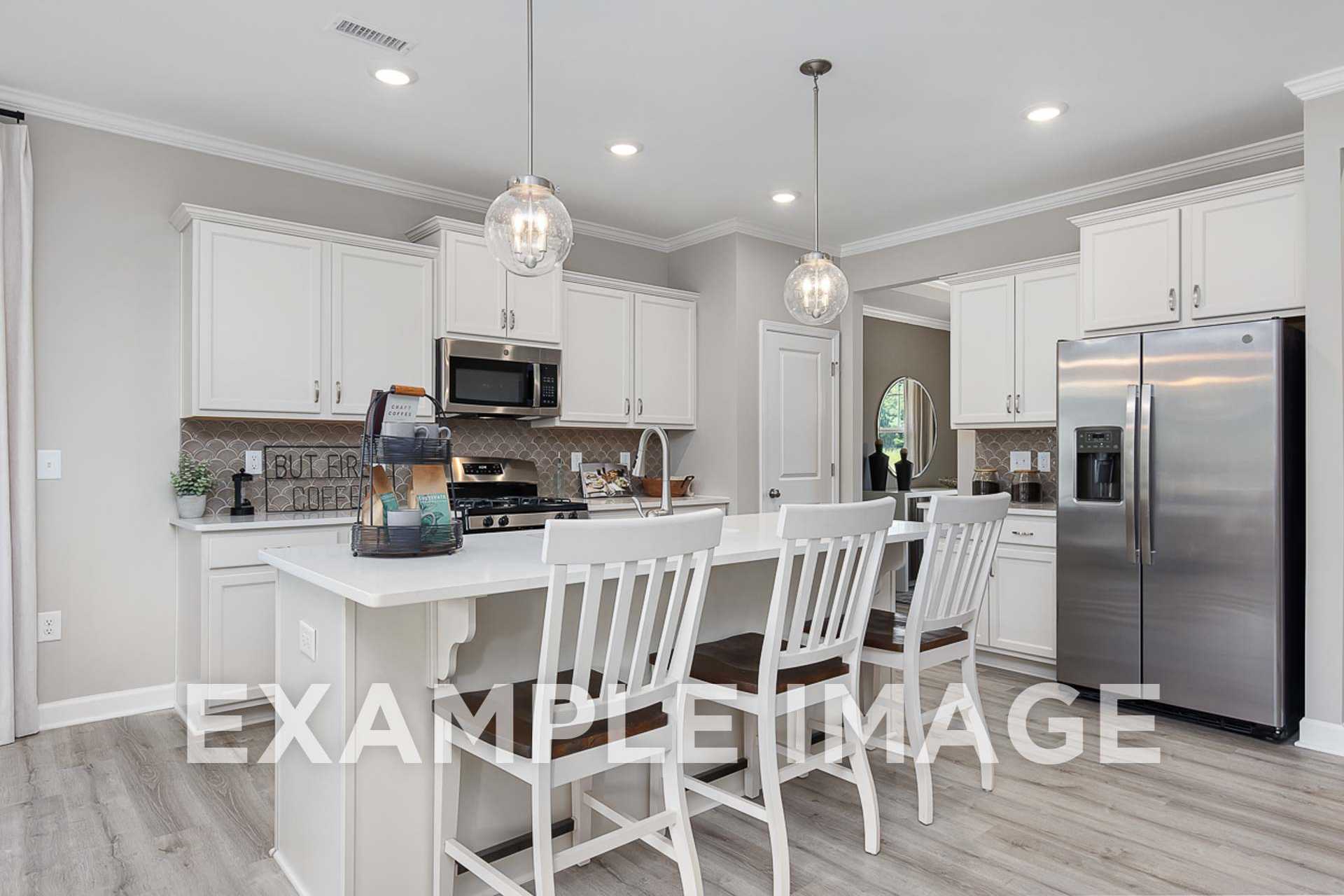 Modern kitchen in The Ash E by Davidson Homes featuring white shaker cabinets, large island, stainless steel appliances, and pendant lights