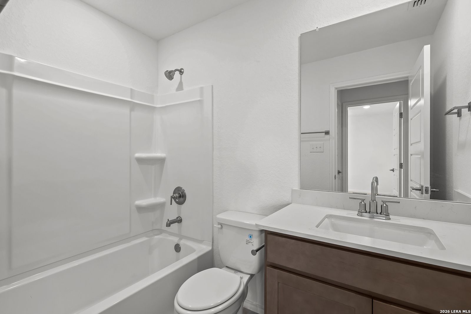 Bright bathroom featuring bathtub-shower combo, wooden vanity, and large mirror in Davidson Homes The Sequoia B, San Antonio
