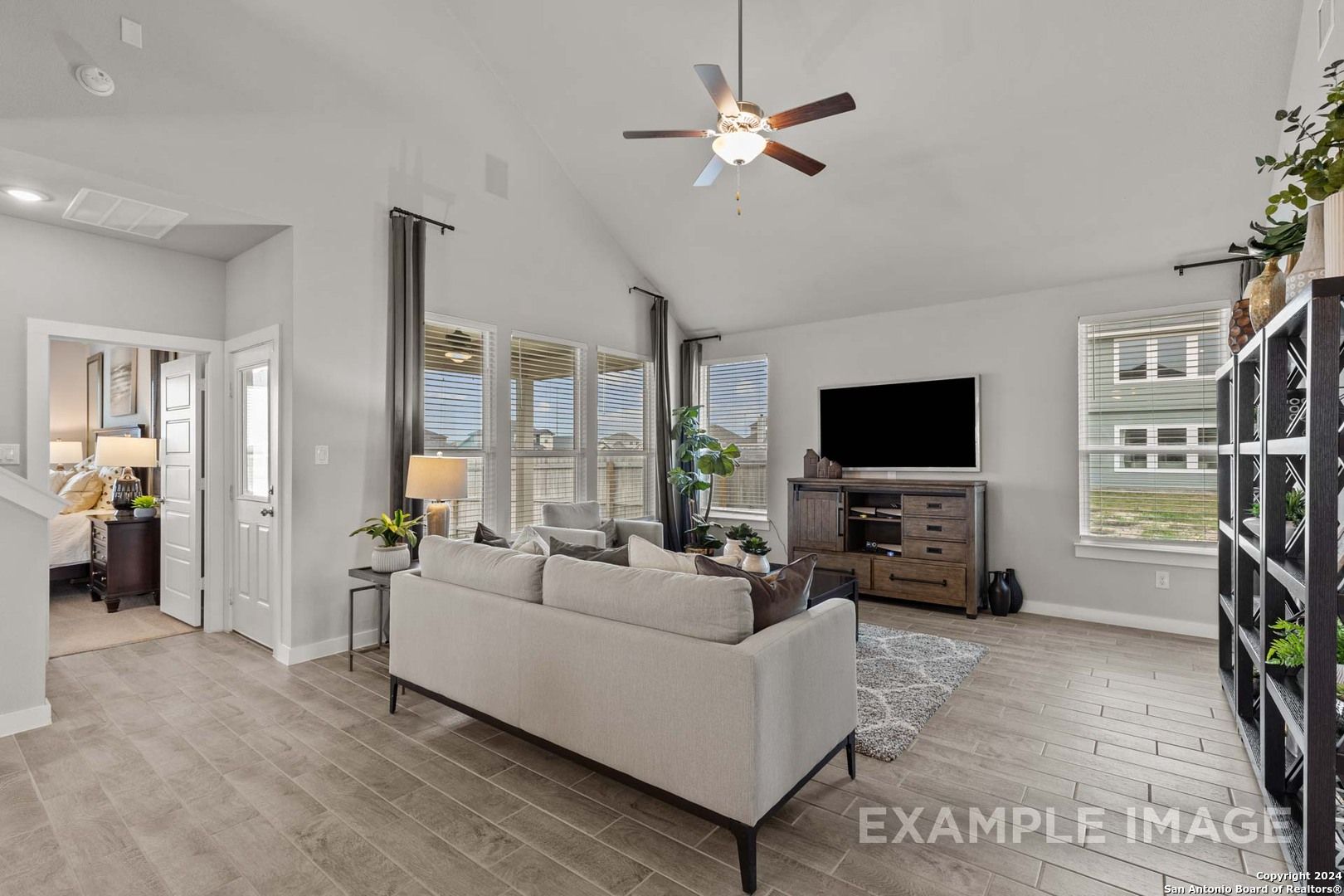 Spacious living room with ceiling fan, large windows, beige sofa, and hardwood floors in The Collin A 3-bedroom home, Seguin, Texas