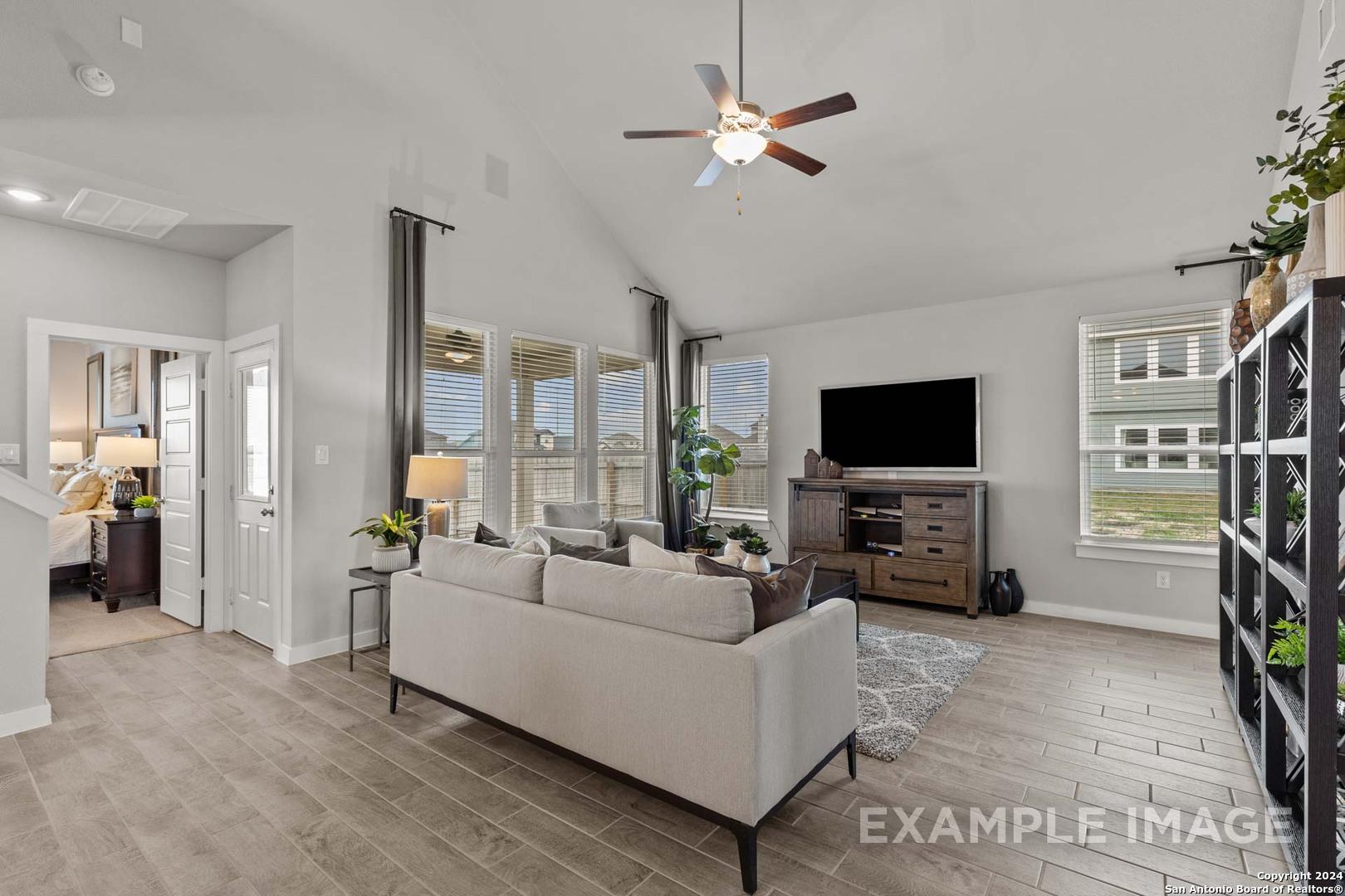 Spacious living room with ceiling fan, large windows, beige sofa, and hardwood floors in The Collin A 3-bedroom home, Seguin, Texas