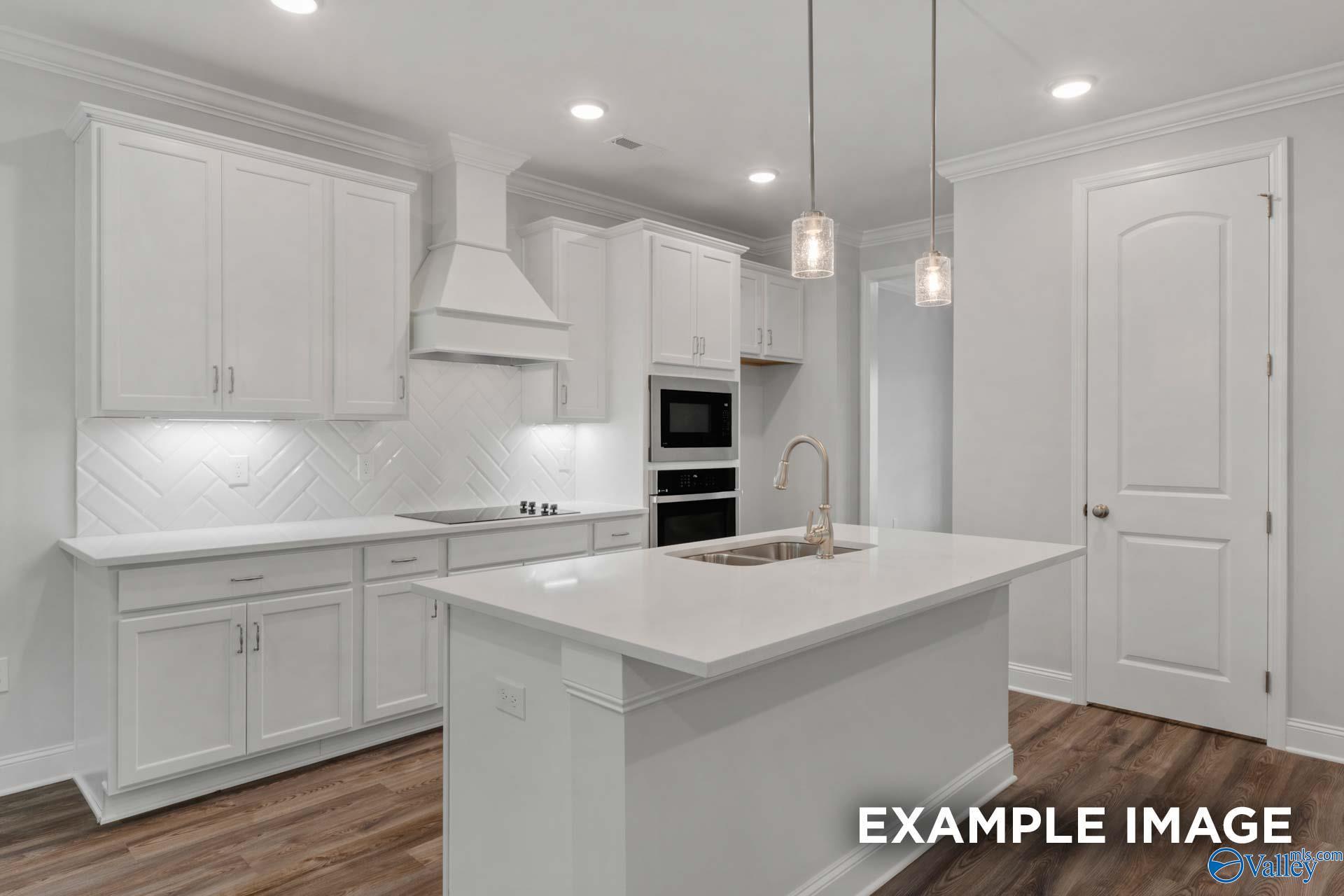 Modern white kitchen with herringbone subway tile backsplash, quartz island sink, stainless double ovens in The Shelby C, Arab, AL