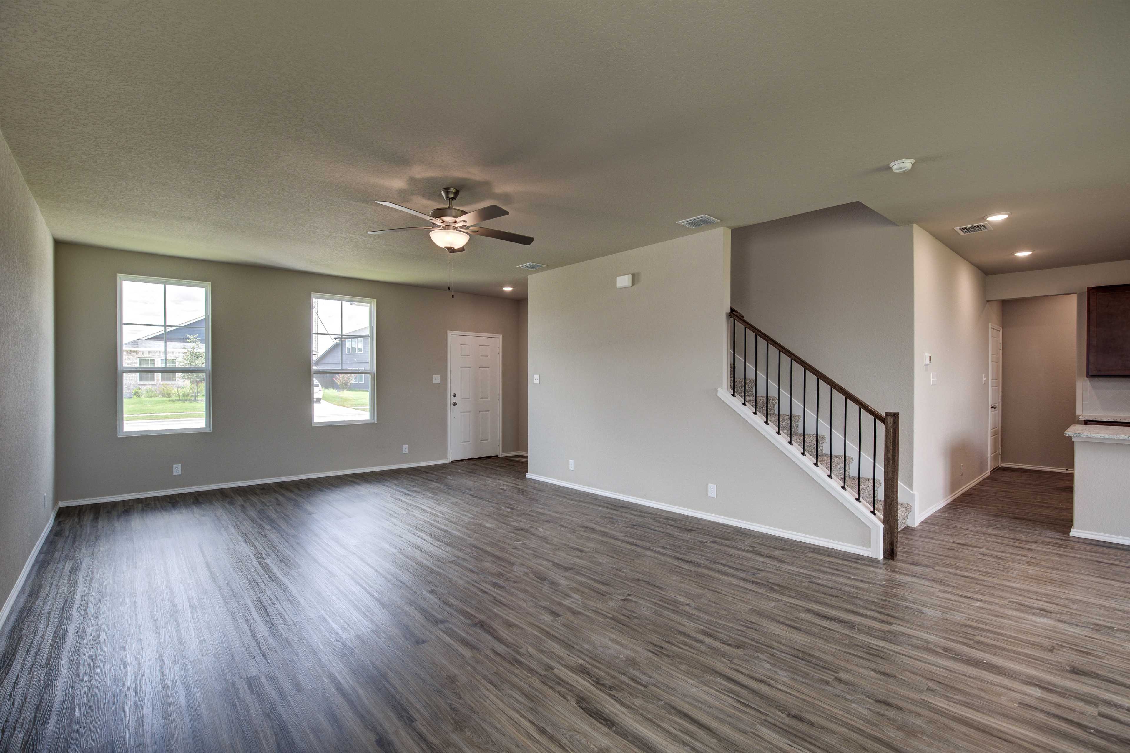 Spacious open-concept living area in The Murray two-story home with hardwood floors, large windows, ceiling fan, and wooden staircase