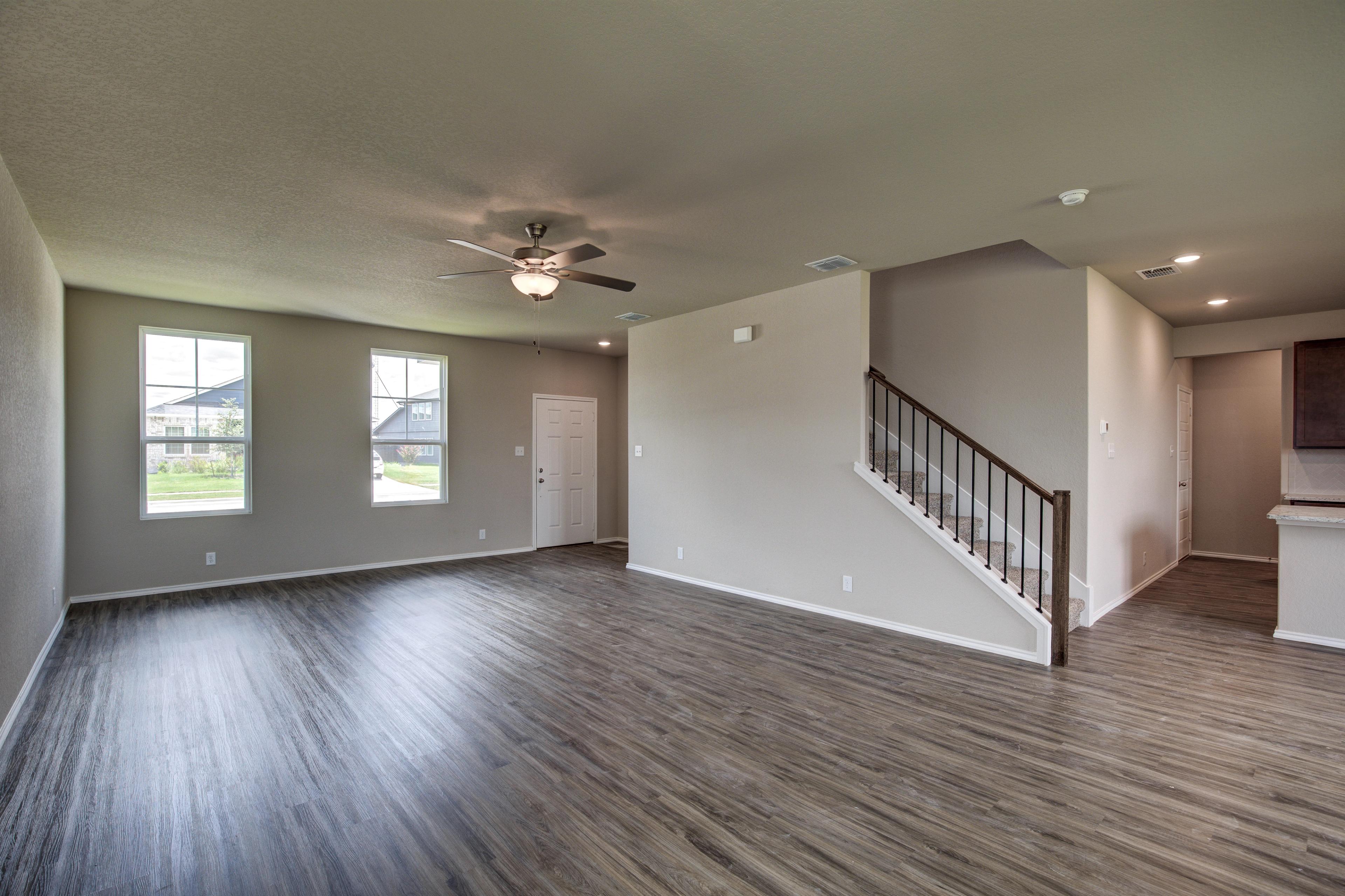 Spacious open-concept living room in The Murray G with hardwood floors, large windows, ceiling fan, and wooden staircase