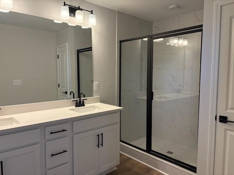 Modern master bathroom with double white vanity, quartz countertop, large mirror, and frameless glass shower in Davidson Homes Cary A, Winder, Georgia