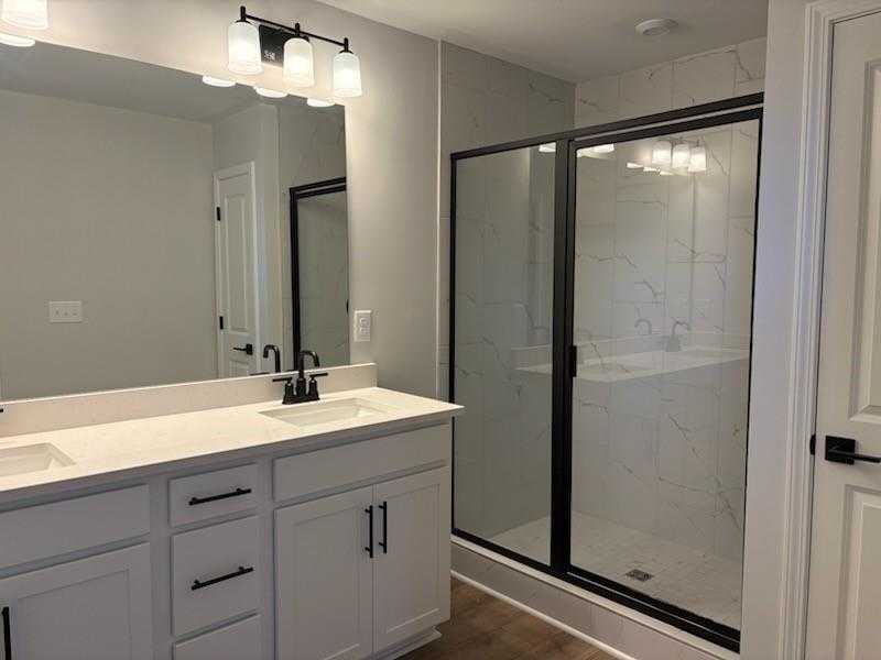 Modern master bathroom with double white vanity, quartz countertop, large mirror, and frameless glass shower in Davidson Homes Cary A, Winder, Georgia