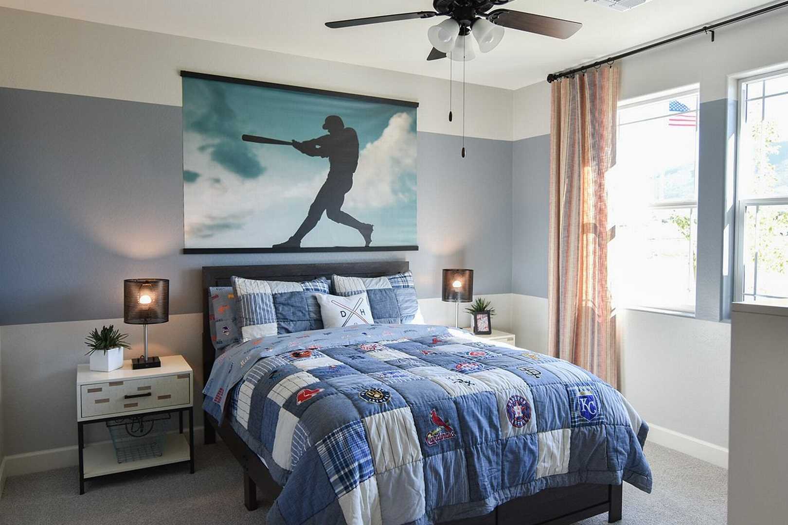 Boy's baseball-themed bedroom in The Summit B by Evermore Homes, with blue quilted bed, sports wall art, and ceiling fan