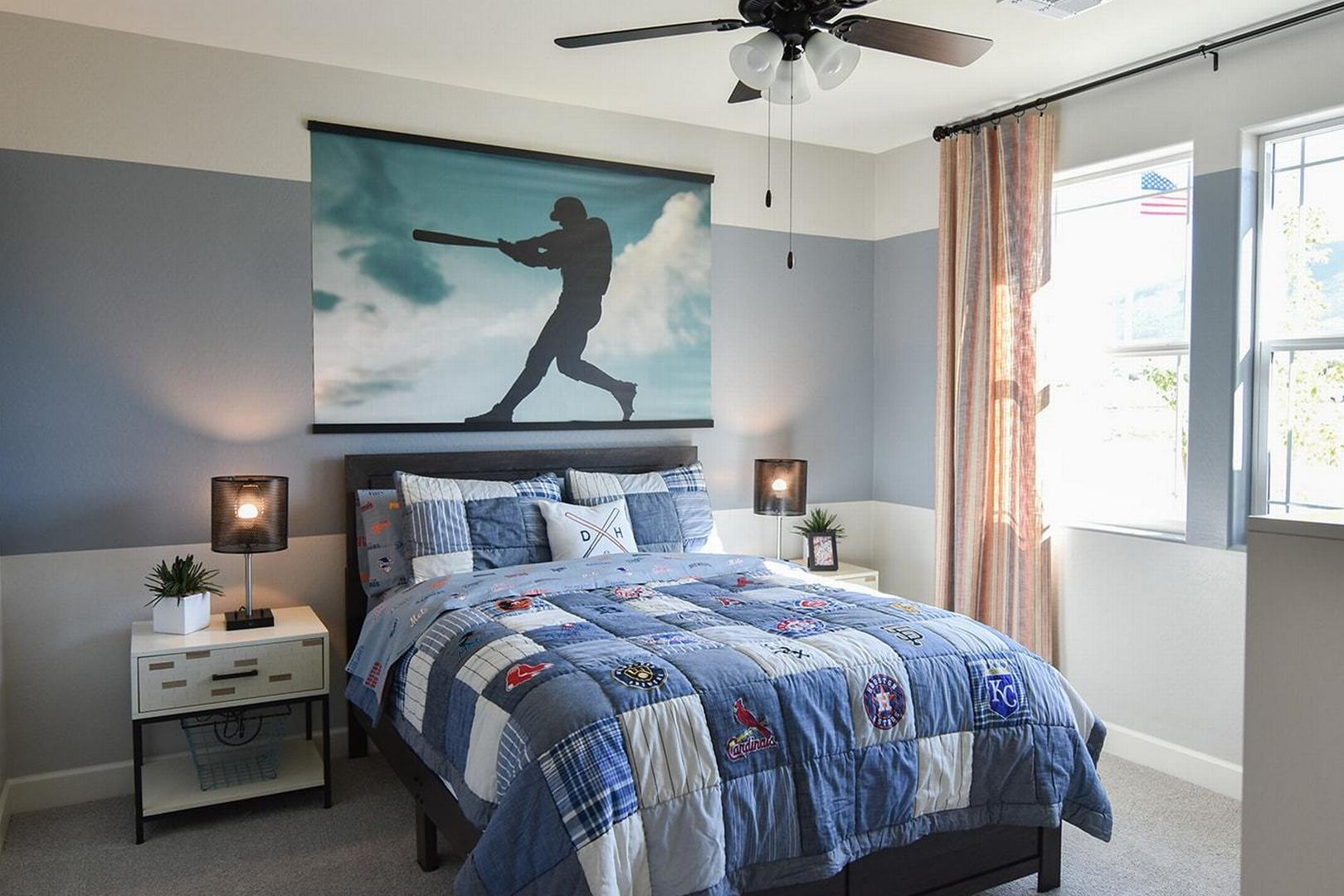 Baseball-themed youth bedroom in The Summit E, Prescott Valley home, with blue quilted bed, sports wall art, nightstands, and ceiling fan