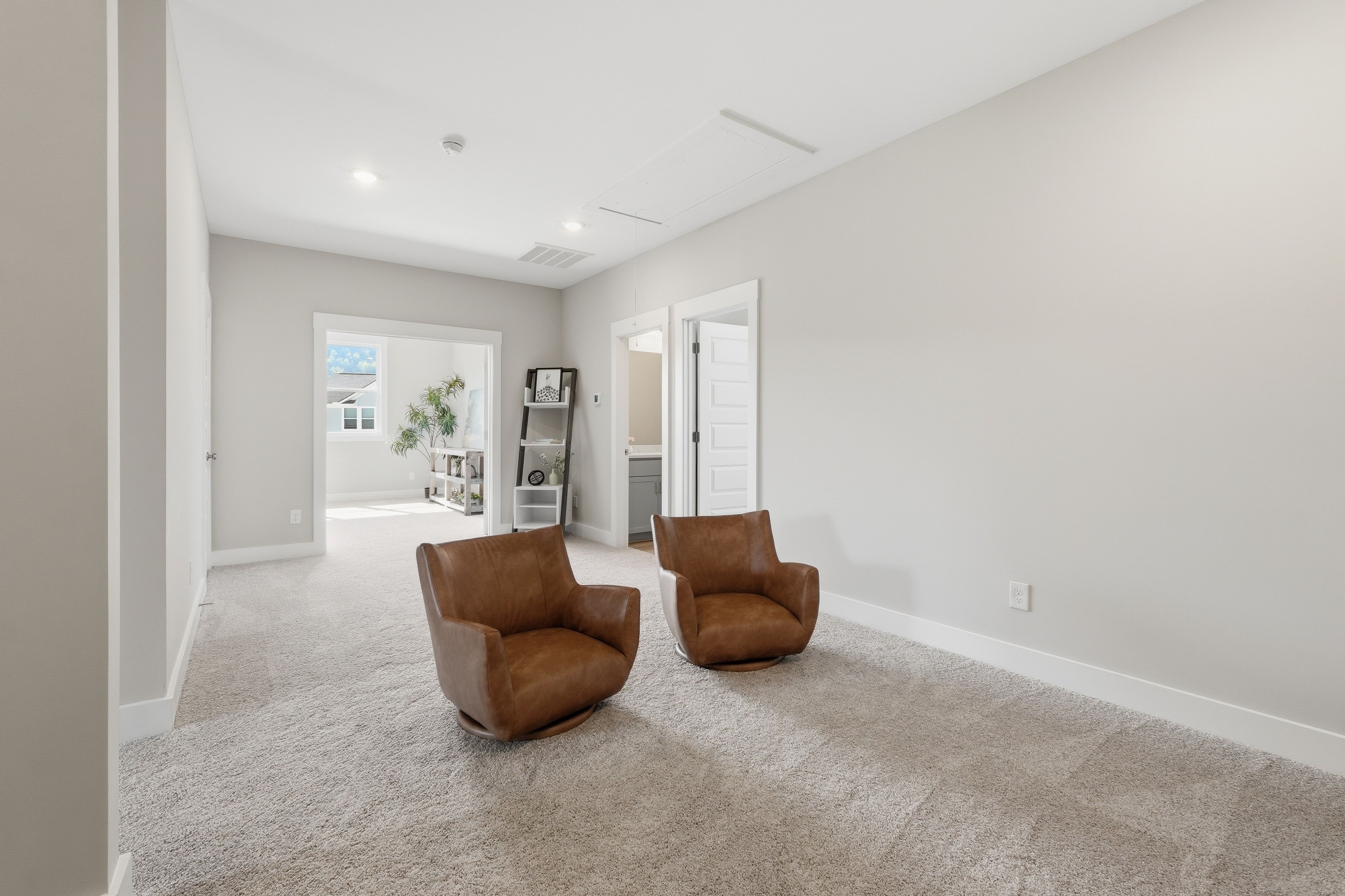 Cozy upstairs seating area with tan leather swivel chairs, open shelving, and neutral walls at The Meadows at Hampton Cove in Owens Cross Roads, Alabama