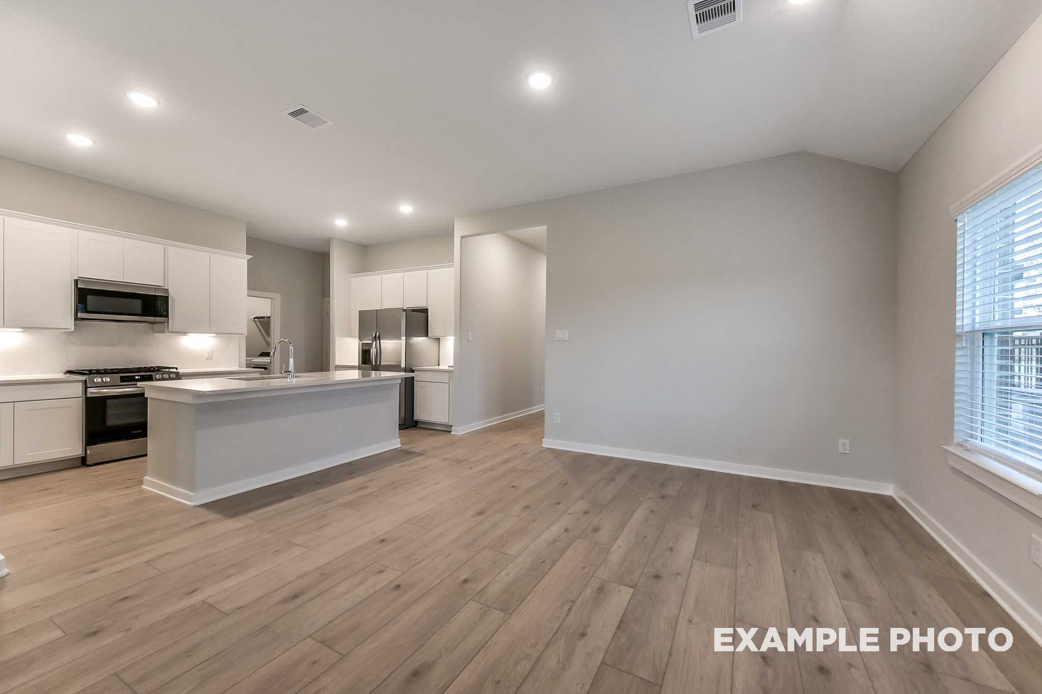 Open-concept kitchen in The Laguna B showcasing white cabinets, stainless steel appliances, large island, and light wood floors