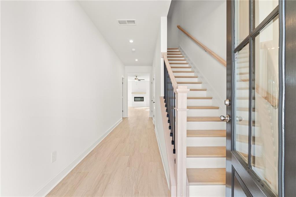 Bright two-story hallway with light oak hardwood floors, modern staircase, and glass-paneled front door in Davidson Homes The Gavin E, Kennesaw, GA