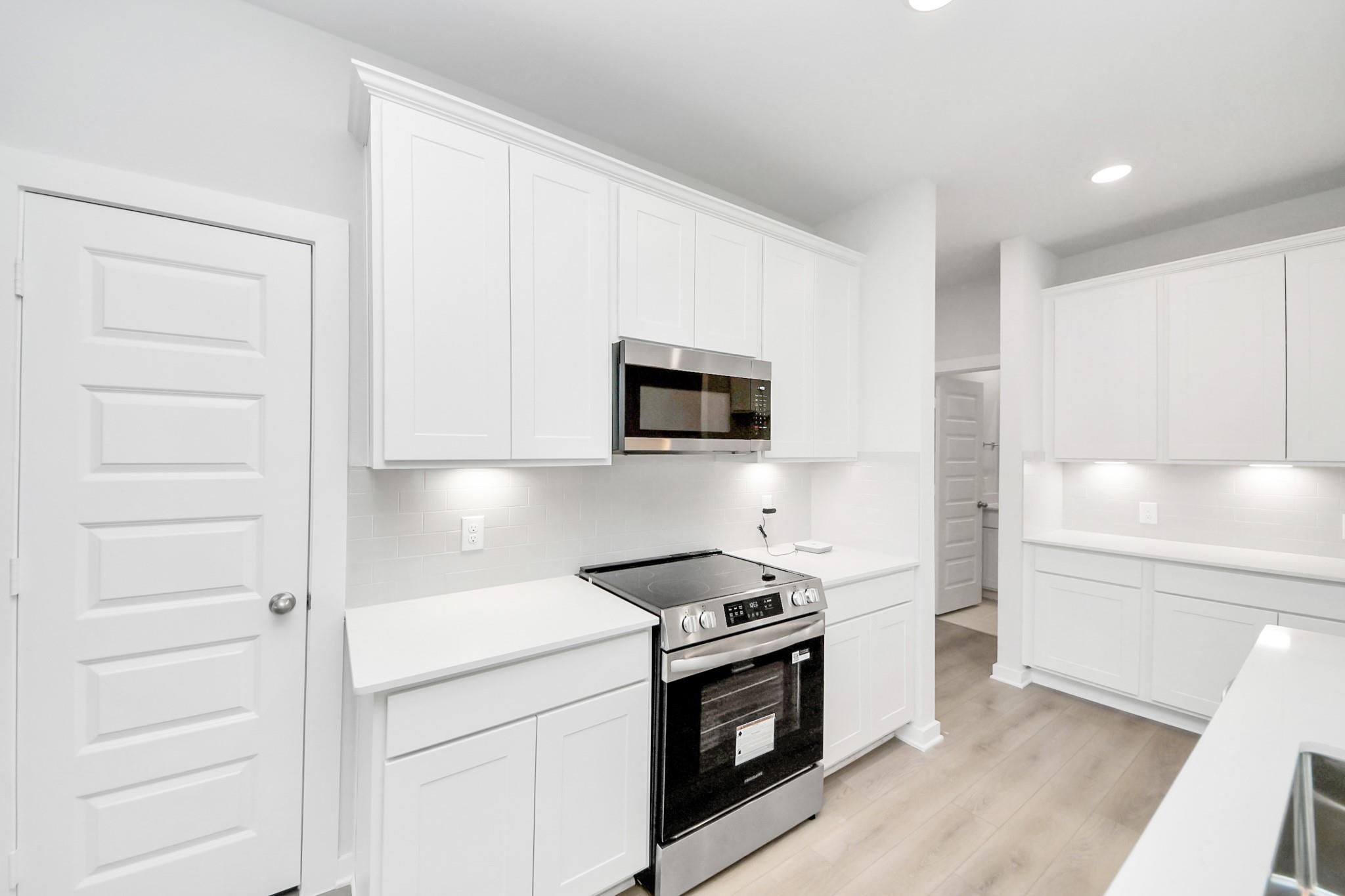 Modern kitchen with white cabinets, stainless steel appliances, and subway tile backsplash in The Frio F, Liberty Estates.