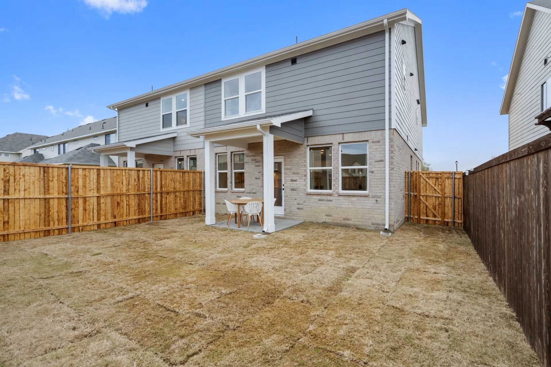 Covered back patio with seating in fenced grassy yard of 2-story Davidson Homes The Wake D, Wylie, Texas