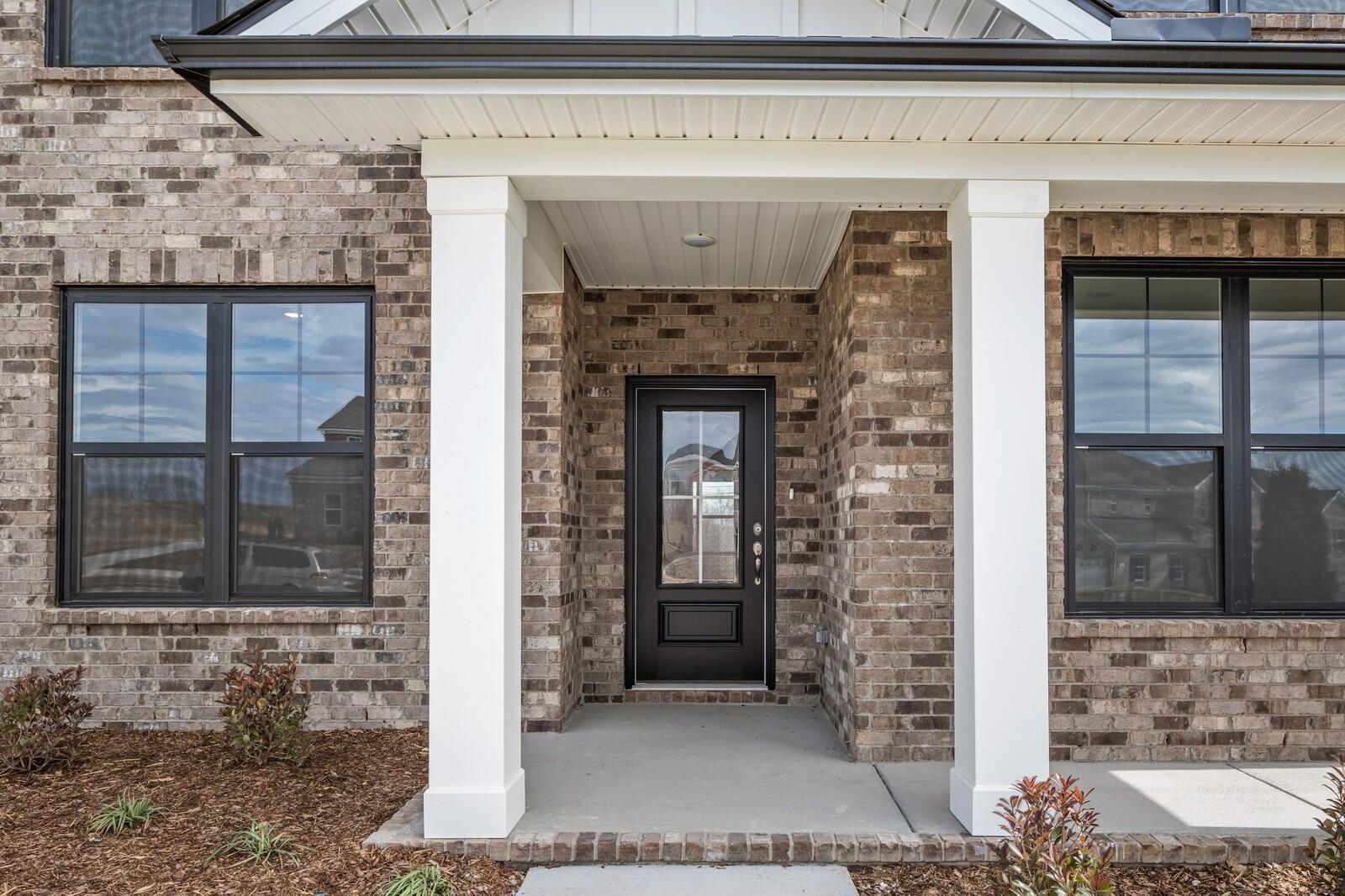 Brick exterior home with covered front porch, white columns, black door, and large windows in Davidson Homes The Ridgeport D, Mt. Juliet, TN
