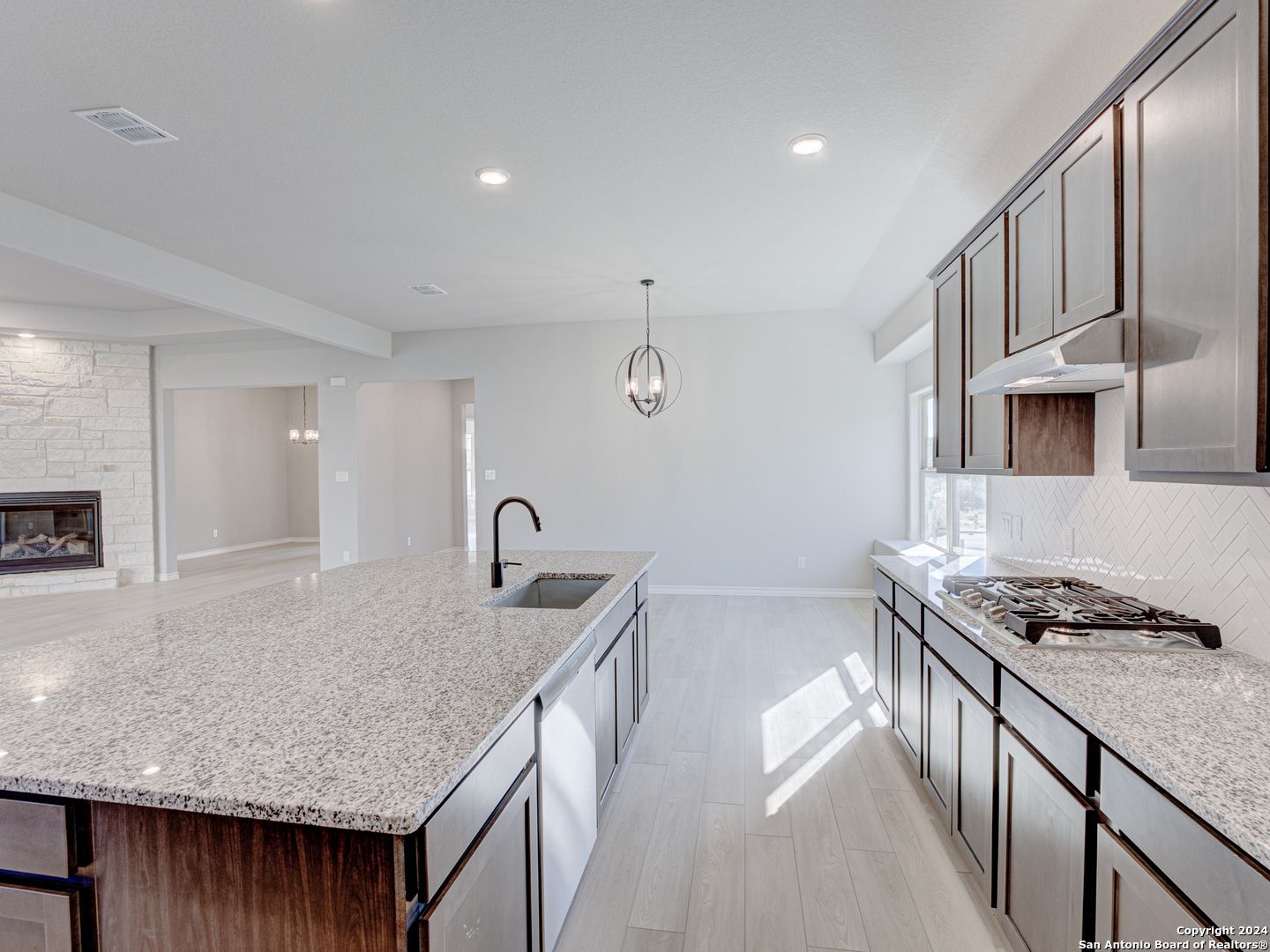 Modern open-concept kitchen with granite island, stainless appliances, and stone fireplace in The Summerlin A, Castroville, Texas