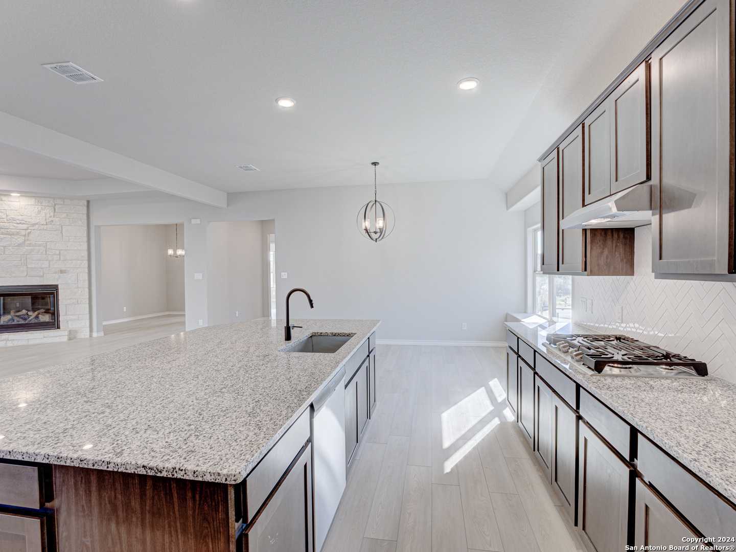 Modern open-concept kitchen with granite island, stainless appliances, and stone fireplace in The Summerlin A, Castroville, Texas