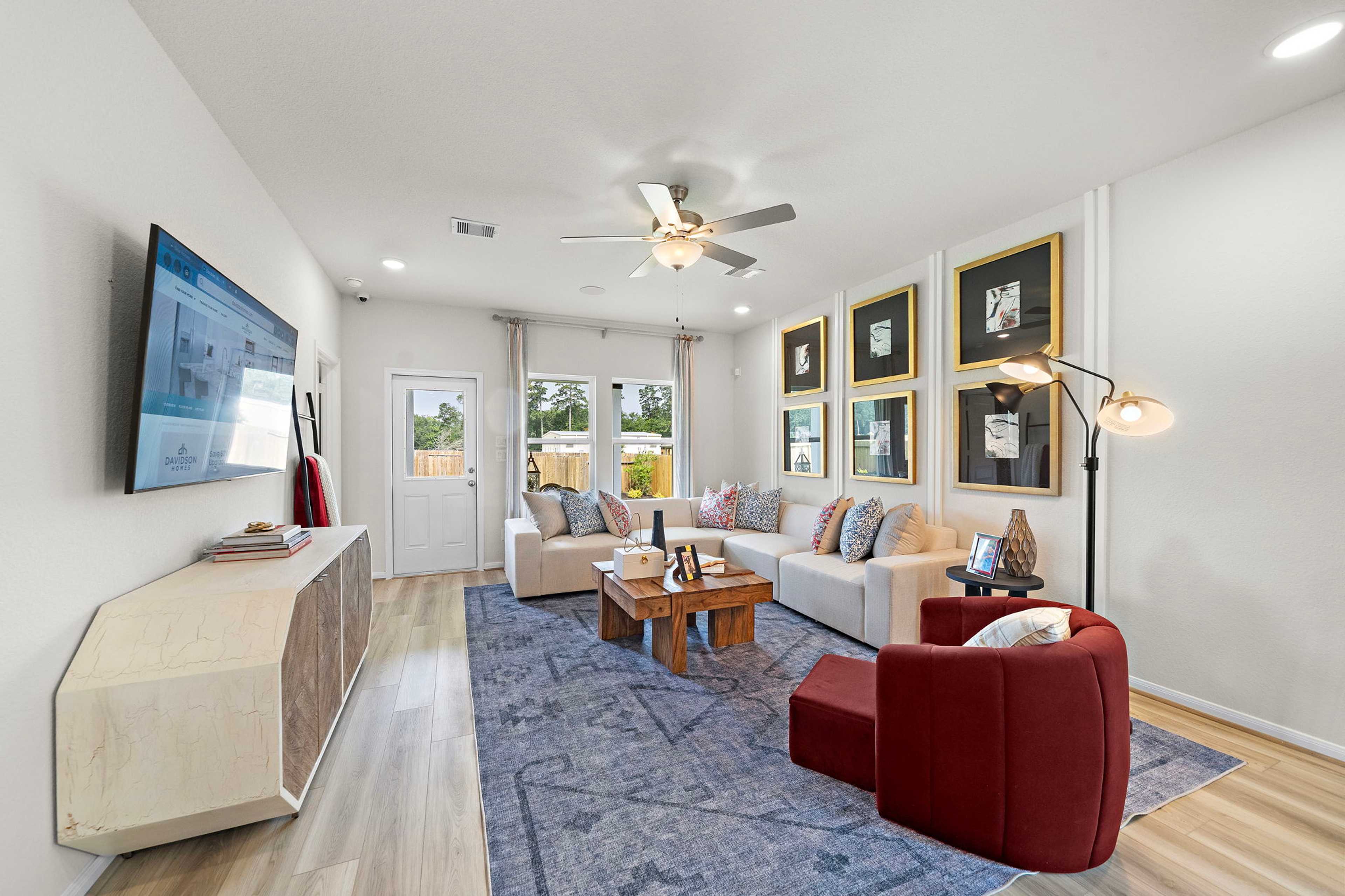 Spacious living room at Liberty Estates in Cleveland Texas with L-shaped sofa, hardwood floors, ceiling fan, wall art, and TV