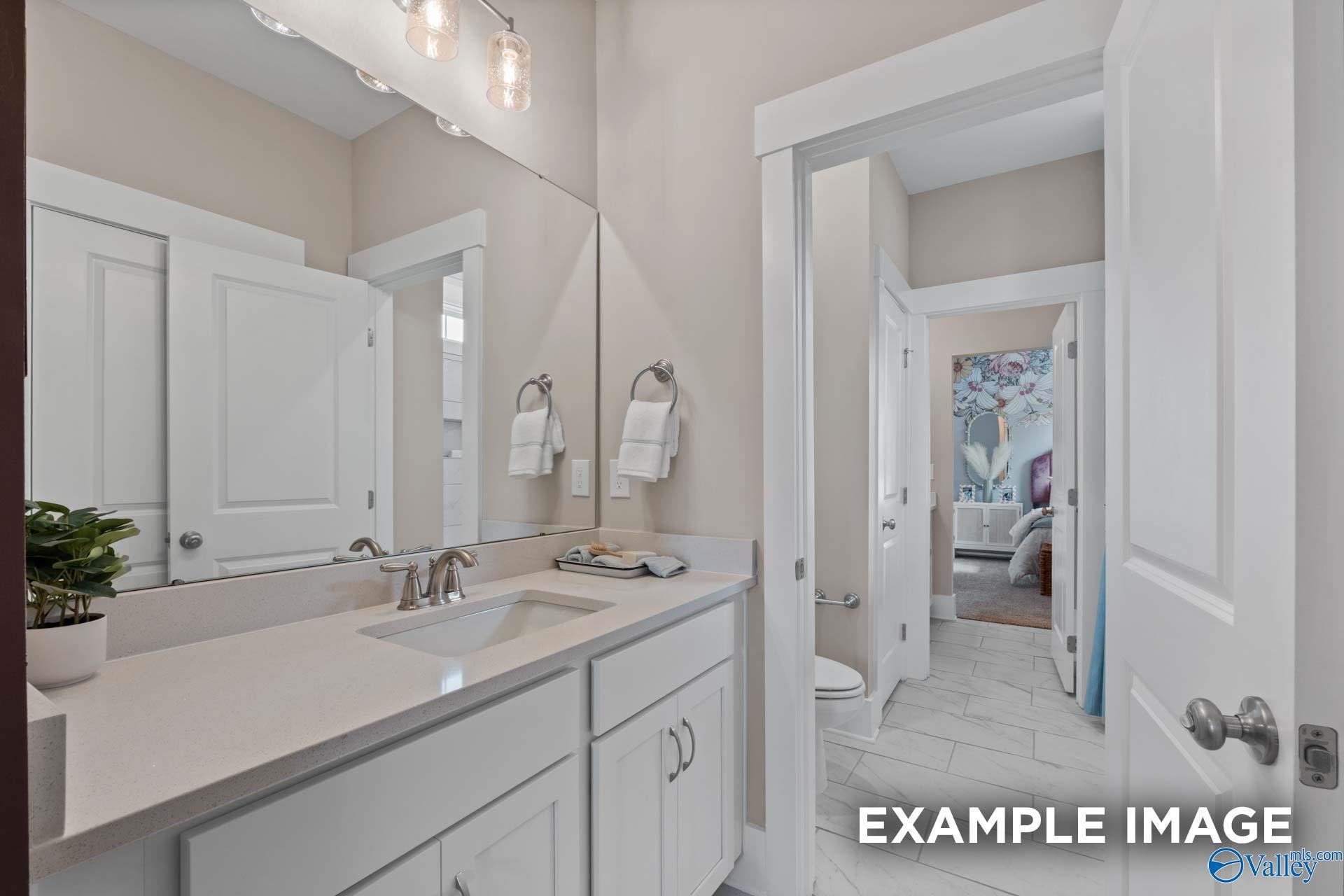 Bright bathroom with white vanity, quartz sink, large mirror, and adjacent bedroom in Davidson Homes The Finleigh, Huntsville AL