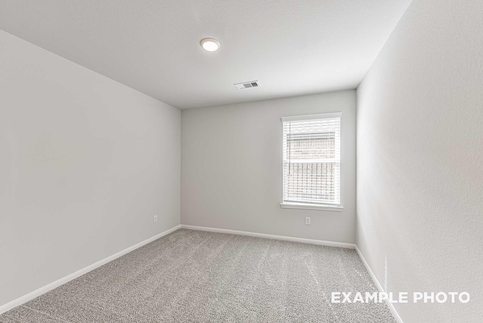 Bright empty bedroom with neutral walls, light gray carpet, large window blinds and recessed lighting in Davidson Homes The Riviera A, Rosharon, Texas