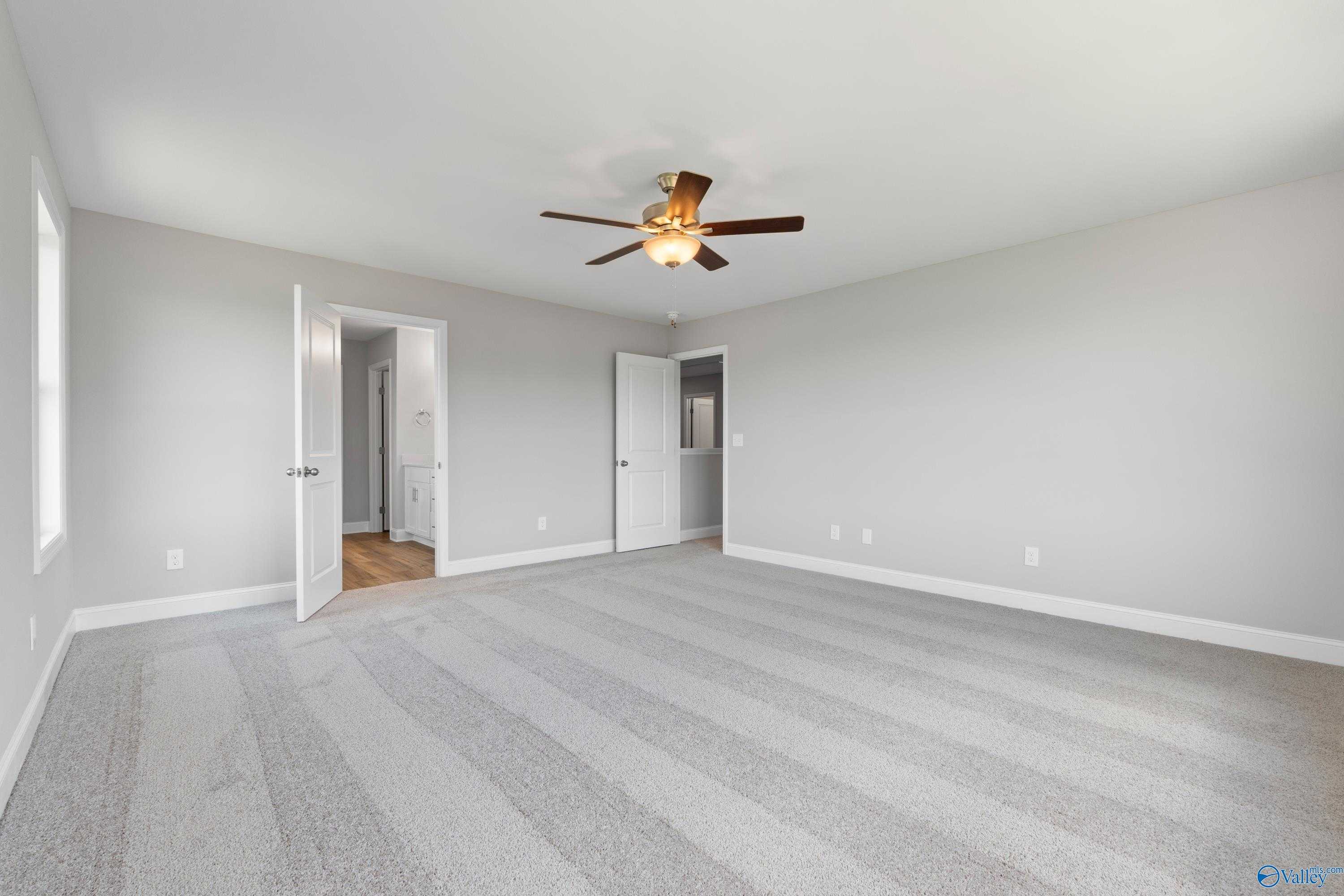 Spacious empty bedroom with light gray walls, beige carpet, ceiling fan, and open doors to bath in Davidson Homes Chelsea B, New Market, AL