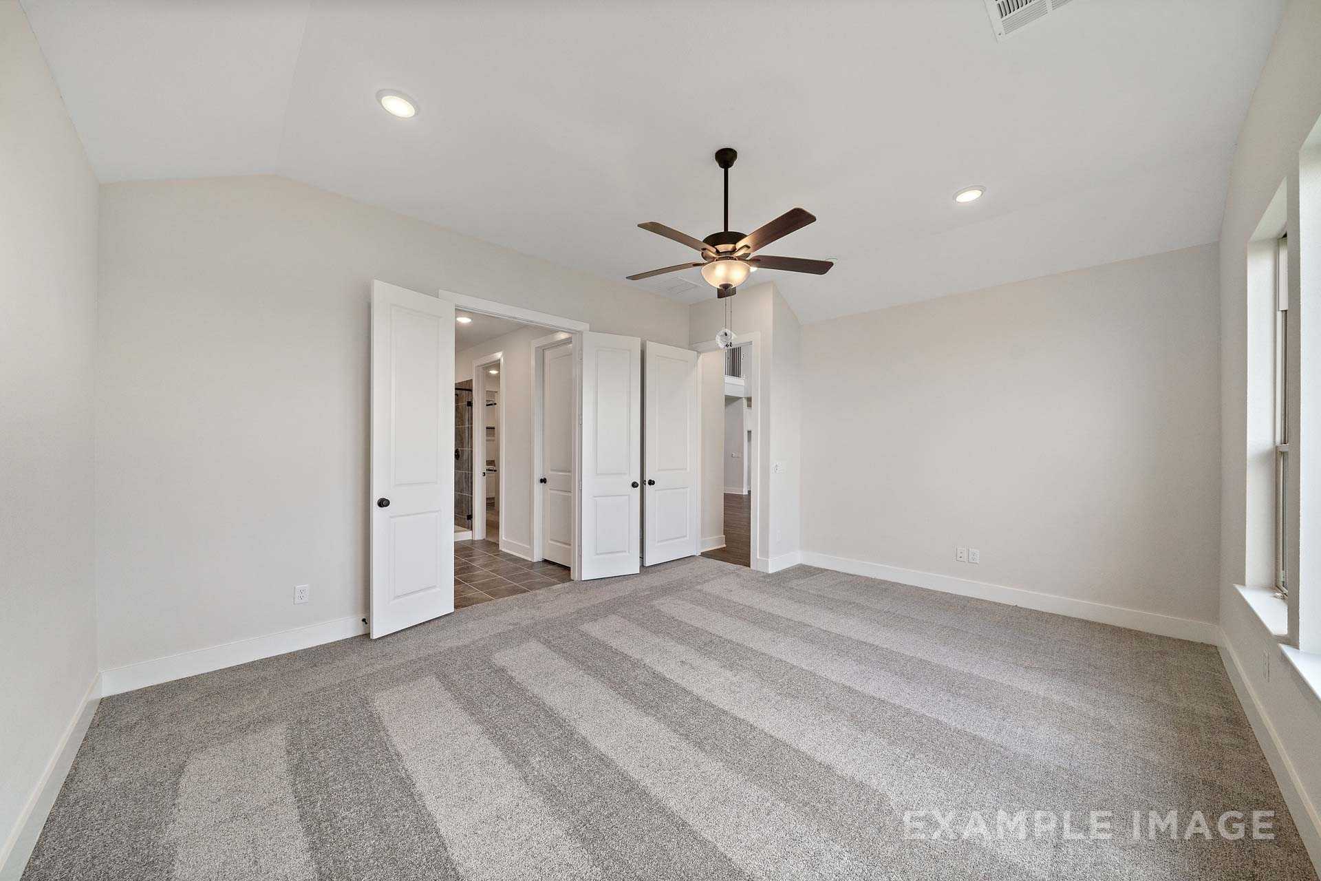 Spacious master bedroom in The Victoria A with beige walls, striped gray carpet, double doors to en-suite, ceiling fan