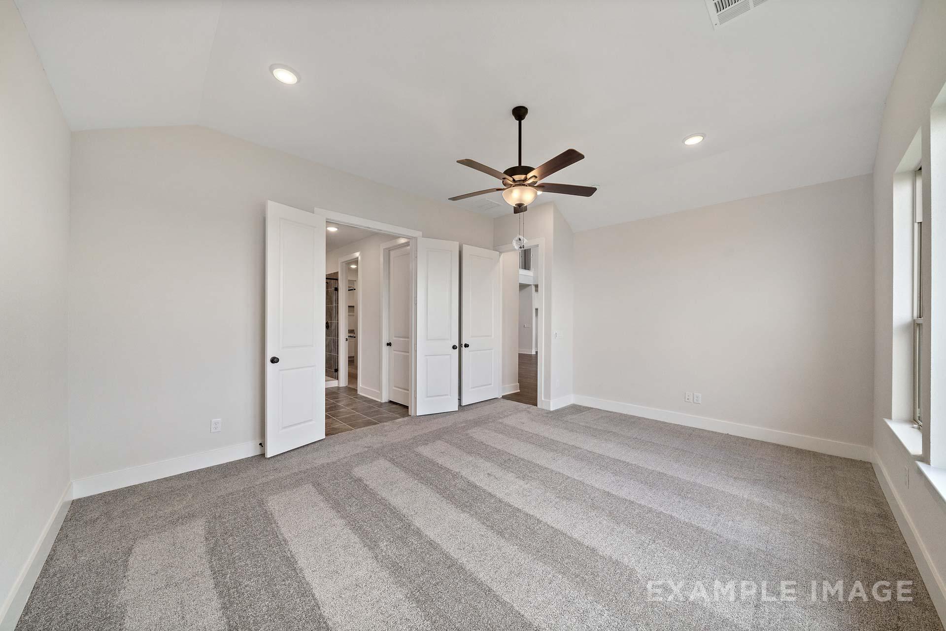 Spacious master bedroom in The Victoria A with beige walls, striped gray carpet, double doors to en-suite, ceiling fan