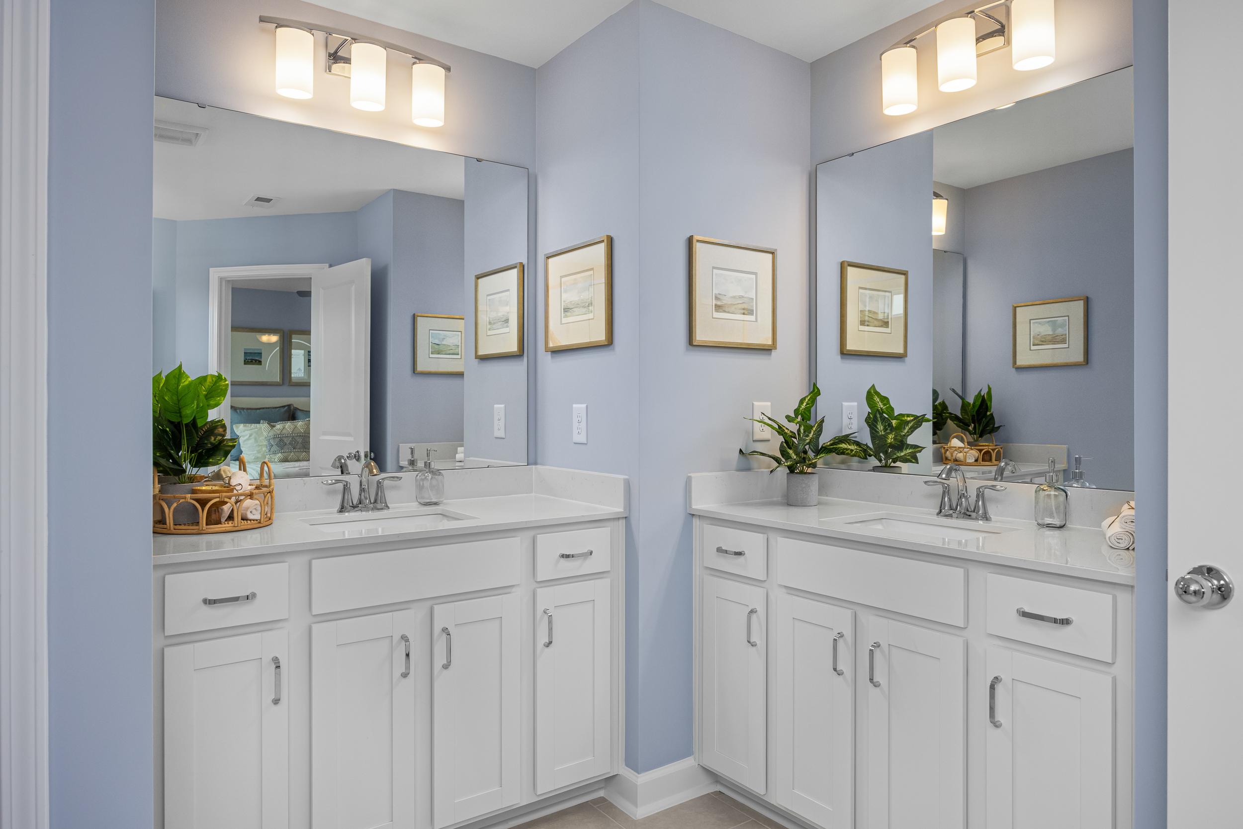Spacious master bathroom at Springvale in Fuquay-Varina NC with dual white vanities, mirrors, blue walls, and potted plants