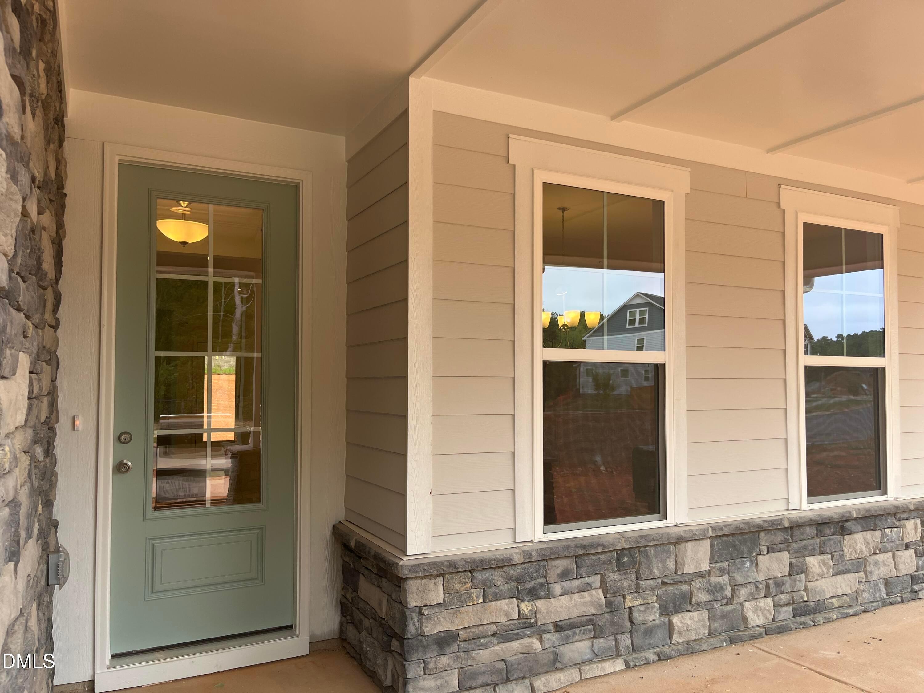 Covered front porch with sage green glass door and stone accents on Davidson Homes The Willow G in Sage on North Main, Wake Forest.
