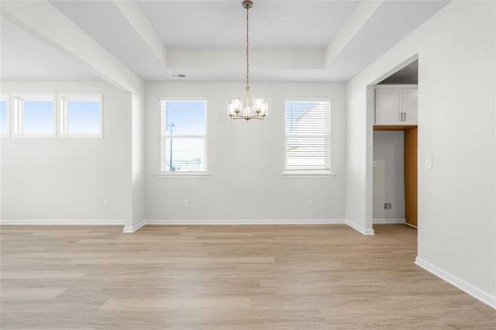 Formal dining room with tray ceiling, chandelier, hardwood floors, and open kitchen in Davidson Homes The Glenwood C at Wehunt Meadows, Hoschton, GA