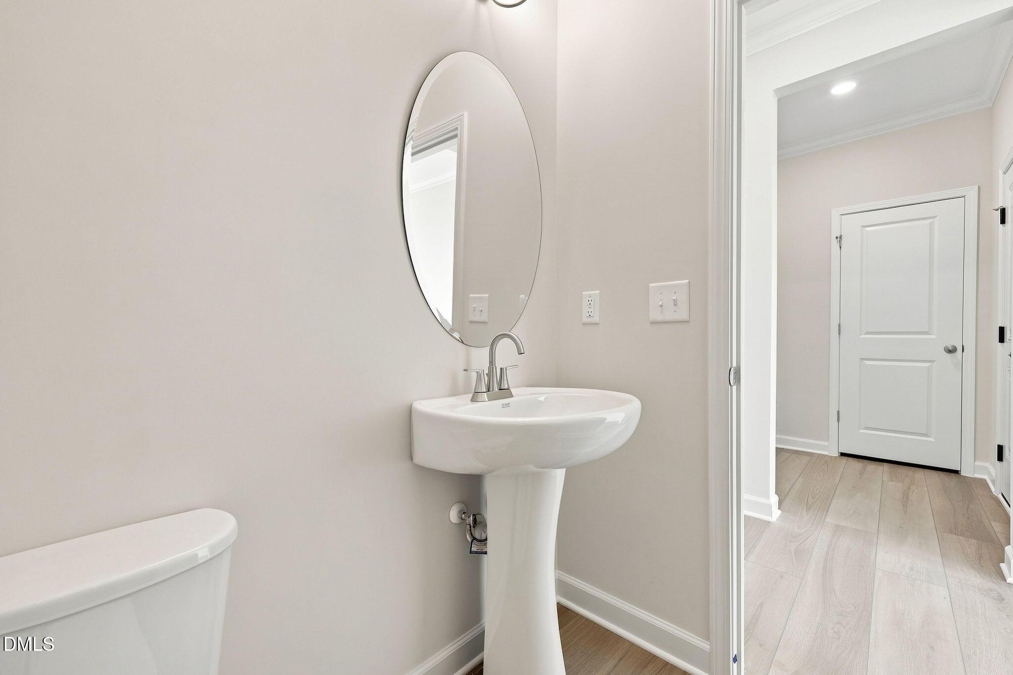 Modern half-bath with pedestal sink and oval mirror in The Magnolia B floor plan at Retreat at North Main, Lillington, NC.