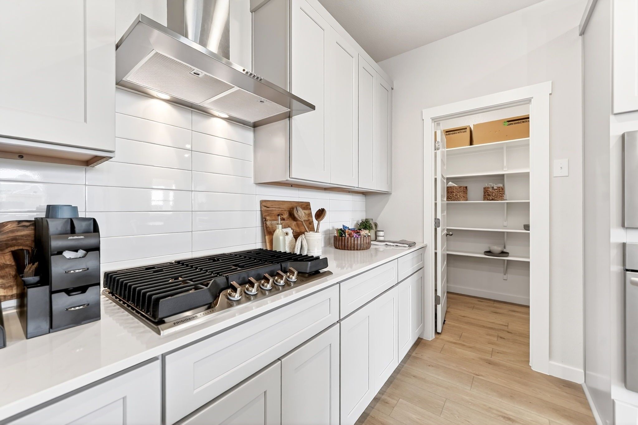 Modern kitchen with gas cooktop, white shaker cabinets, and walk-in pantry in The Laurel I home in Heartland, Texas.