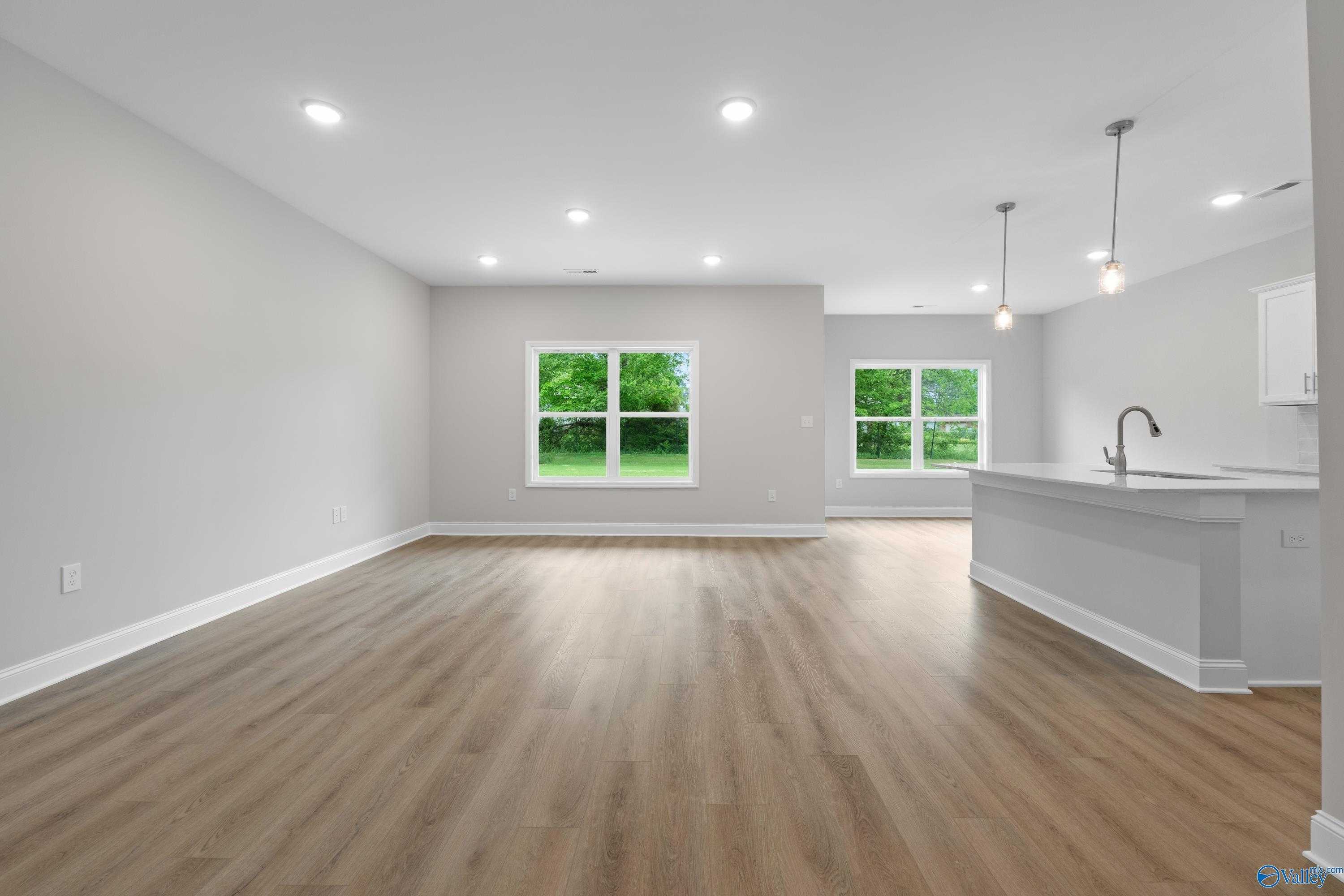 Open-concept living room with hardwood floors, large windows, and adjacent white kitchen island in The Asheville C, Huntsville AL