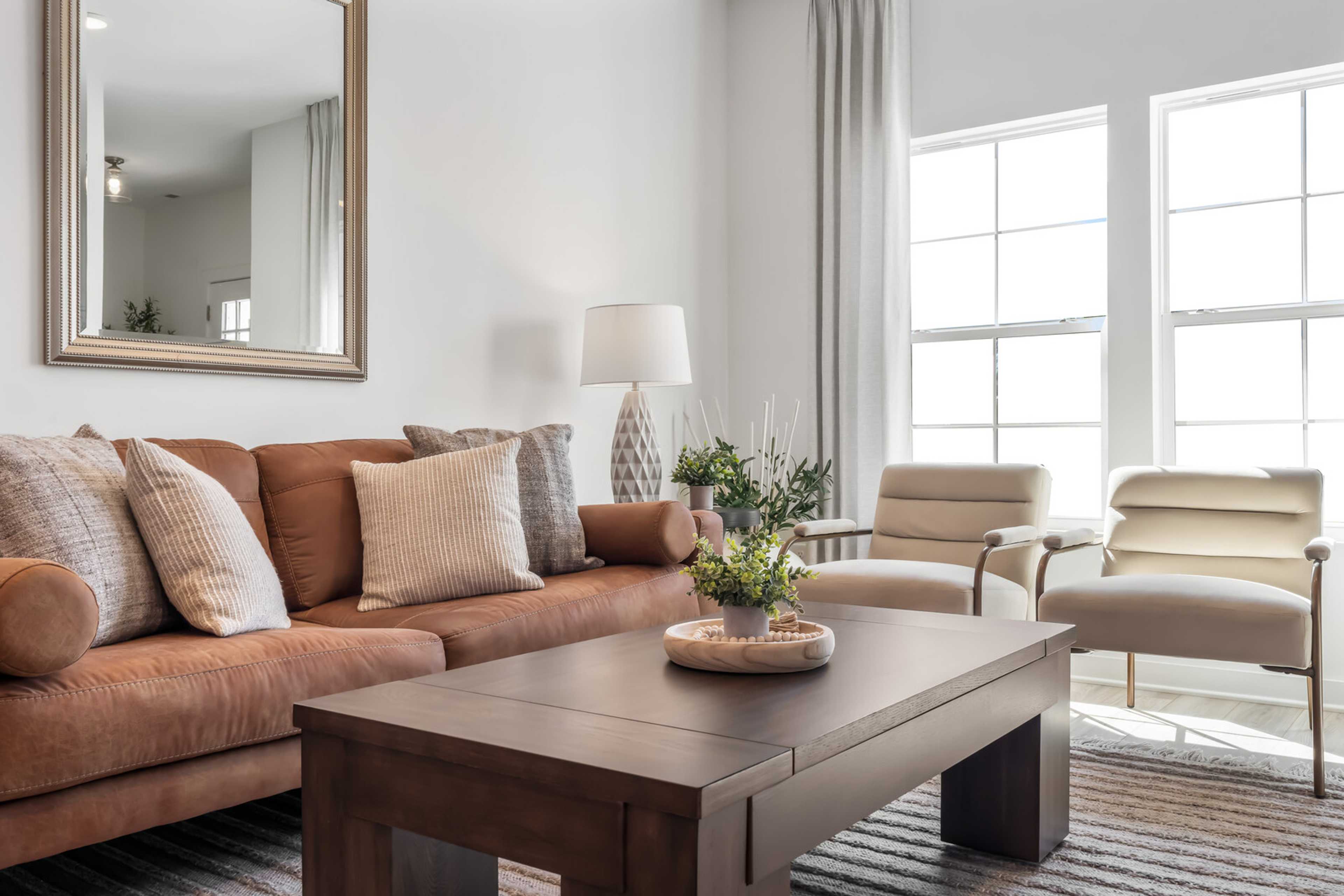 Modern living room at The Towns at Red River in Gallatin TN with tan leather sofa, cream armchairs, wooden coffee table, plants, and large sunny windows