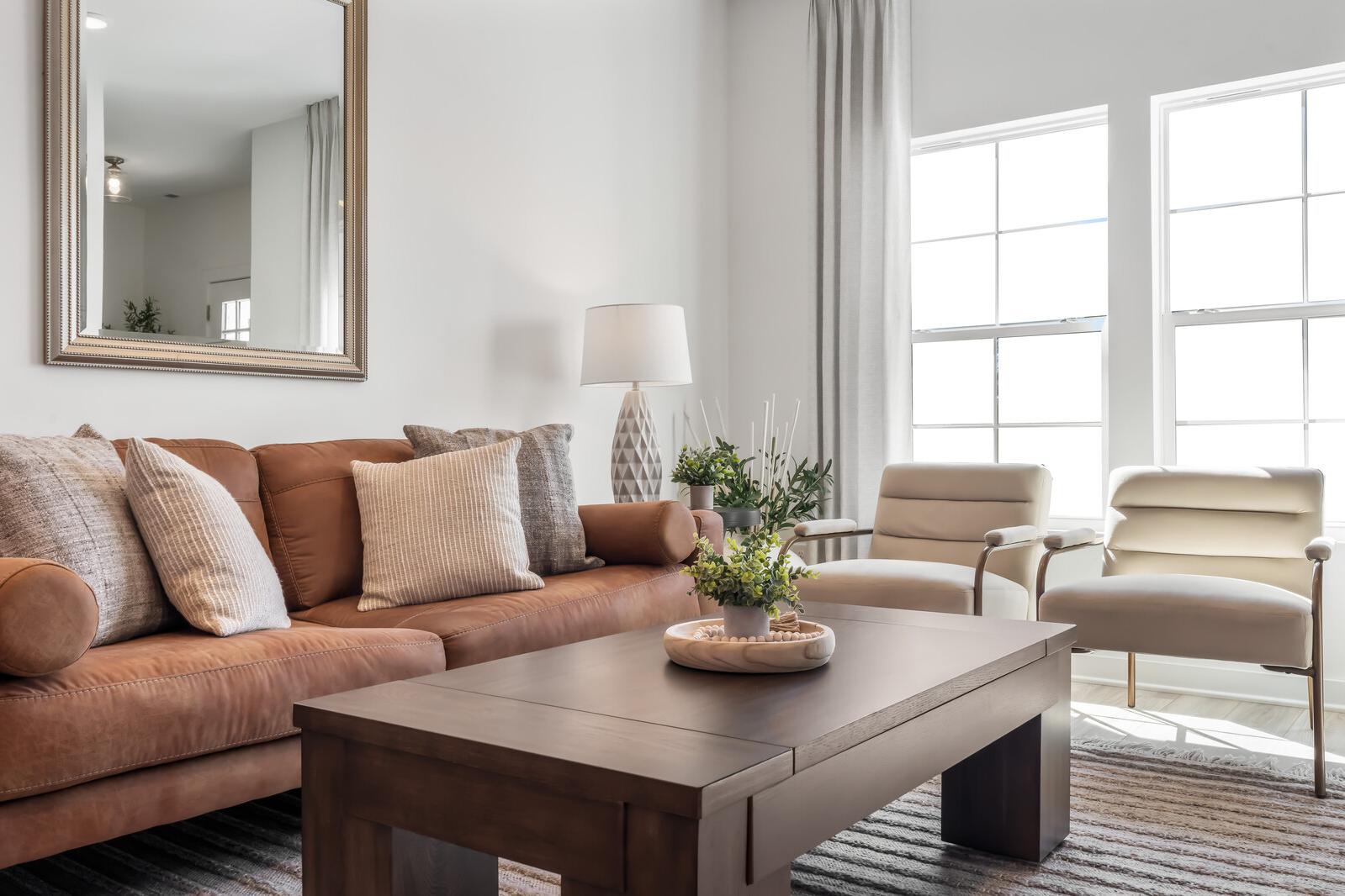 Modern living room at The Towns at Red River in Gallatin TN with tan leather sofa, cream armchairs, wooden coffee table, plants, and large sunny windows