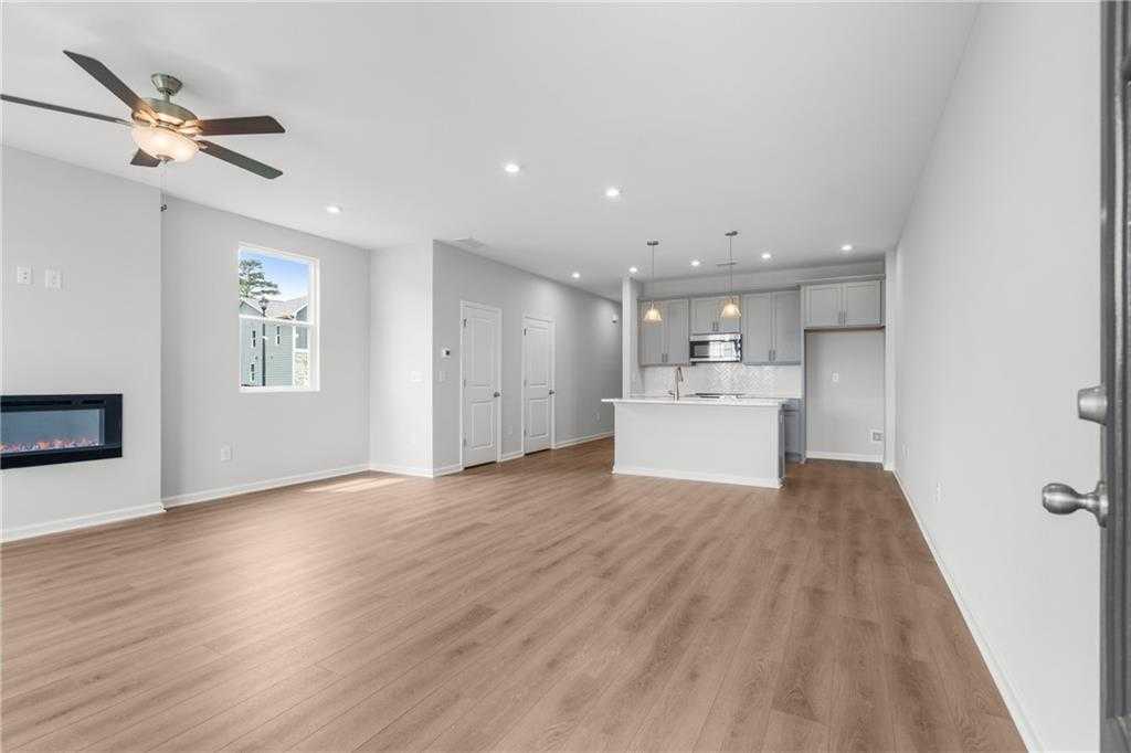 Spacious open-concept living room and kitchen with gas fireplace, hardwood floors, and ceiling fan in Davidson Homes The Monroe A, Emerson, Georgia