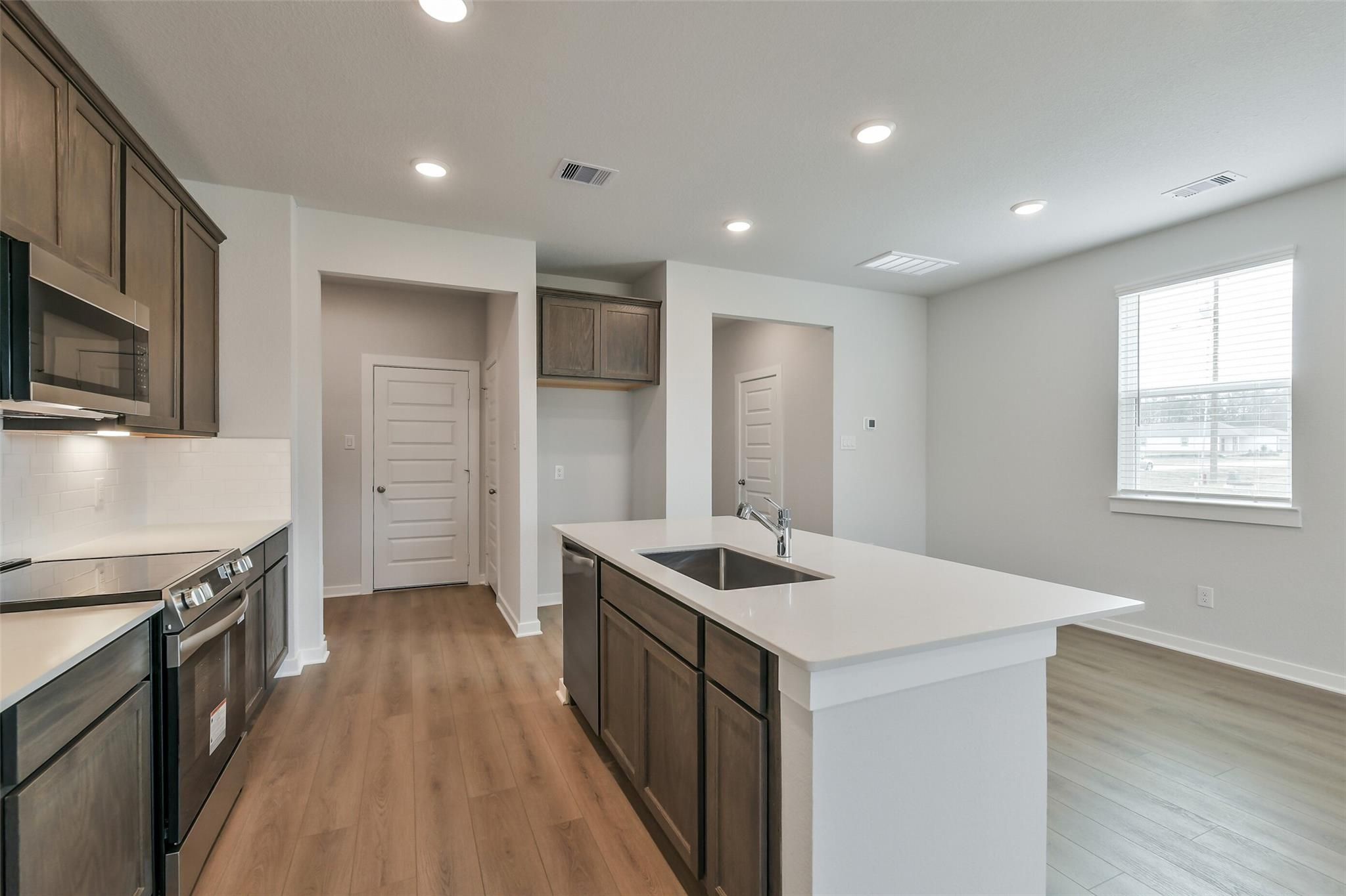 Modern open-concept kitchen with white quartz island, stainless steel appliances, and hardwood floors in The Brazos E, Cleveland, Texas