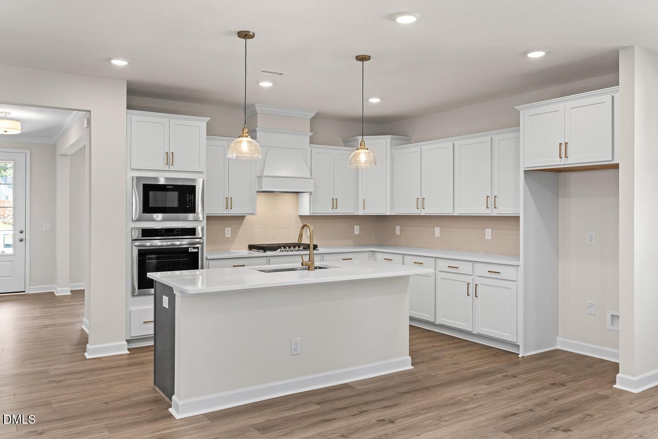Modern white kitchen with island, pendant lights, and stainless appliances in Davidson Homes The Birch II C, Wake Forest, NC