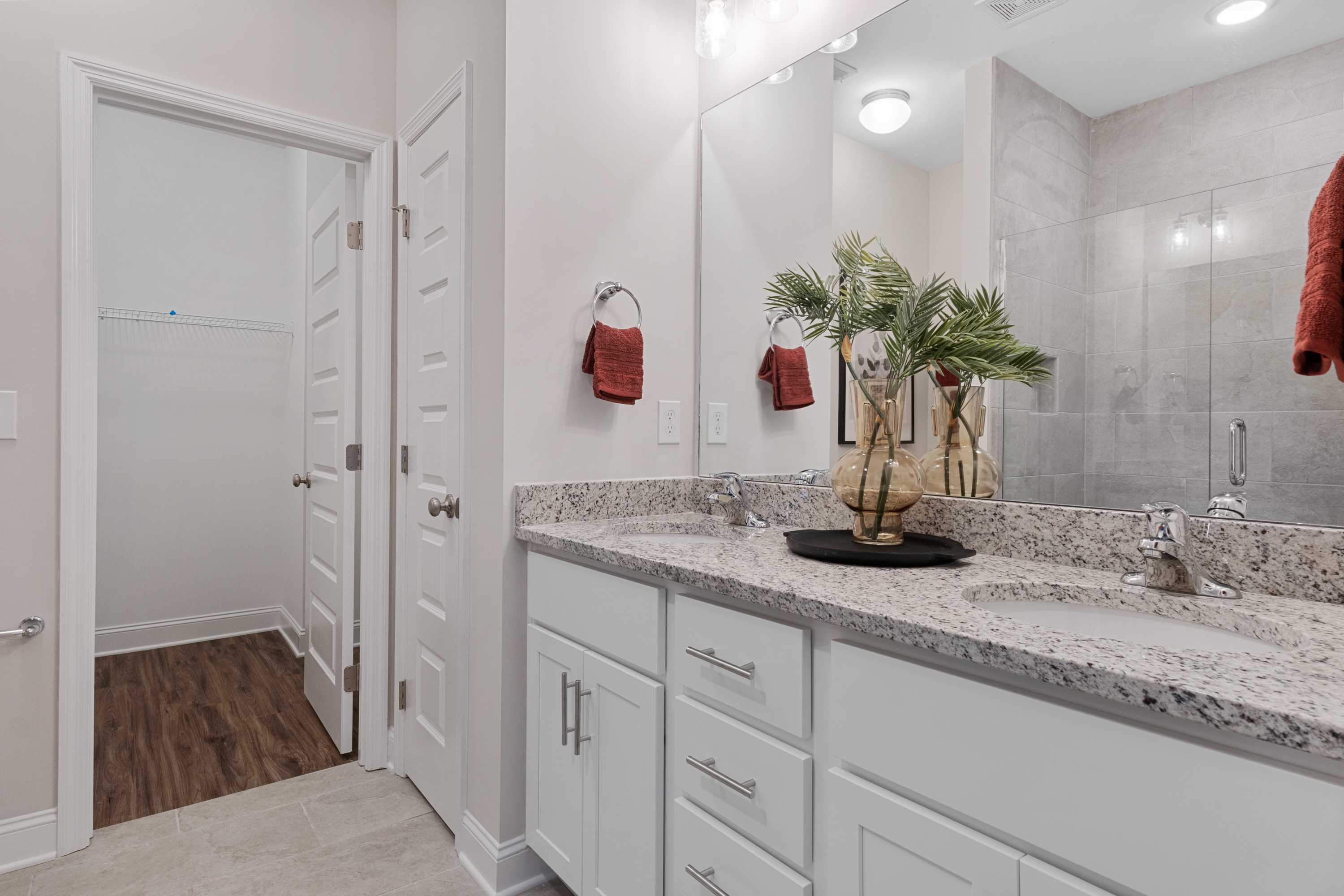 Modern bathroom at The Retreat at Cain Park in Hartselle Alabama with white vanity, quartz countertop, potted plant, and glass shower