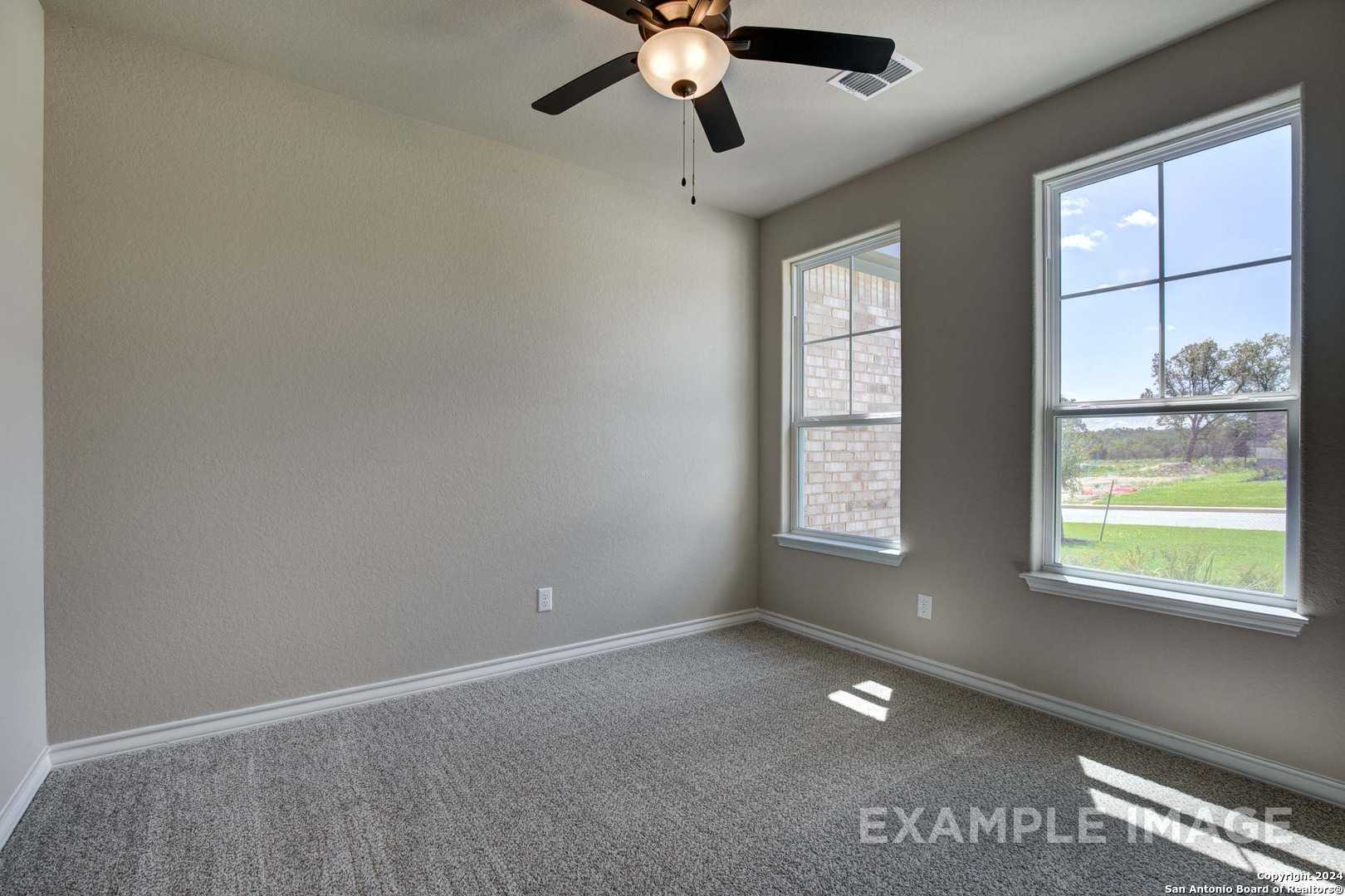 Bright bedroom with neutral walls, carpet flooring, ceiling fan, and windows viewing lush greenery in Davidson Homes The Rockford G, Ladera, San Antonio