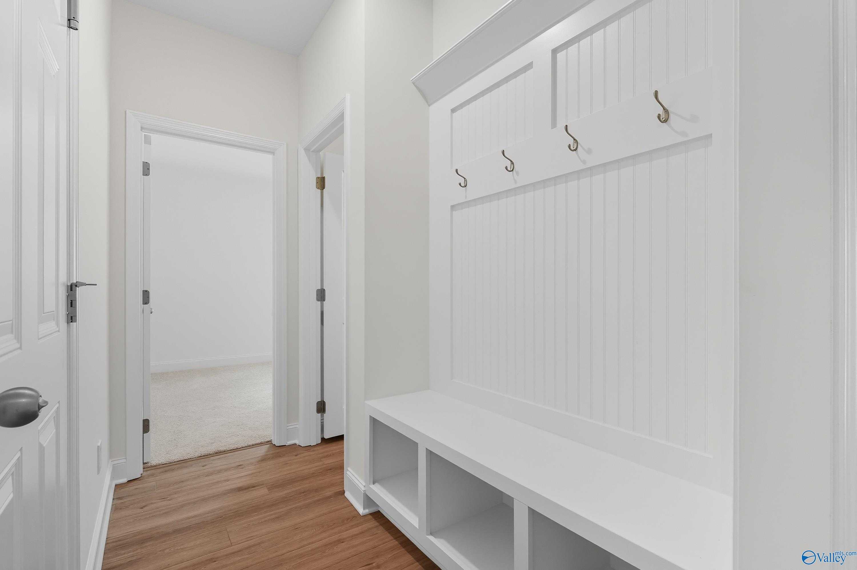 White built-in mudroom with coat hooks, storage bench, and hardwood floors in Davidson Homes The Everett, Meridianville, Alabama