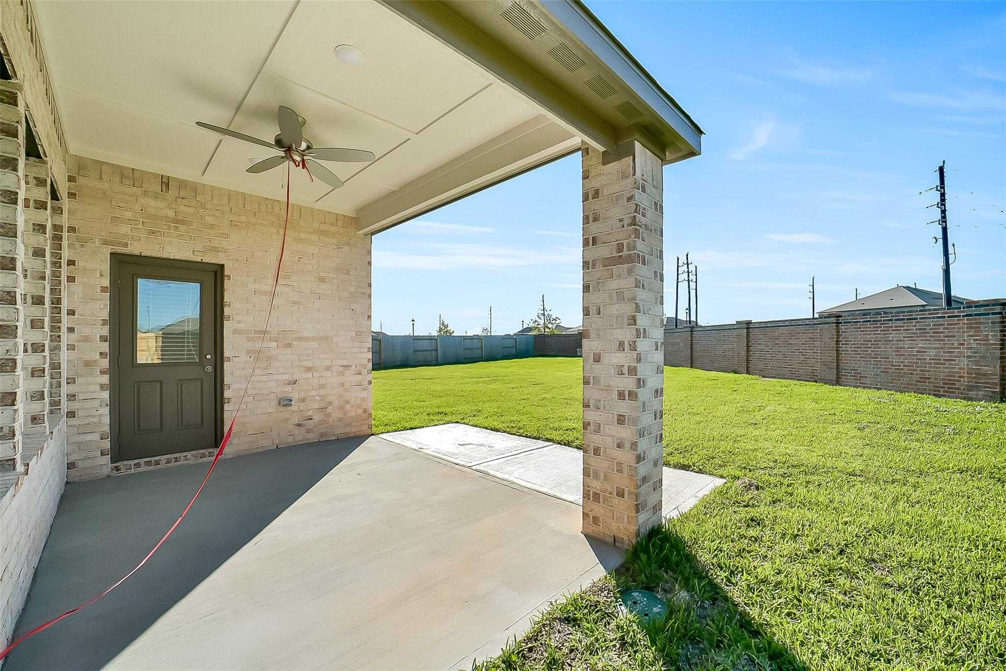 Covered back patio with ceiling fan, brick columns, and lush green backyard in Davidson Homes The Acadia A, Sunterra, Katy, Texas