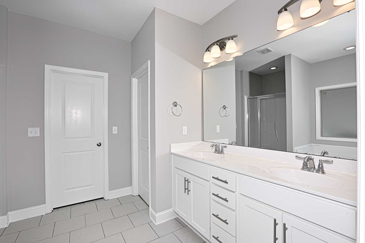 Spacious master bathroom in The Montgomery with double white vanity, gray walls, and glass shower