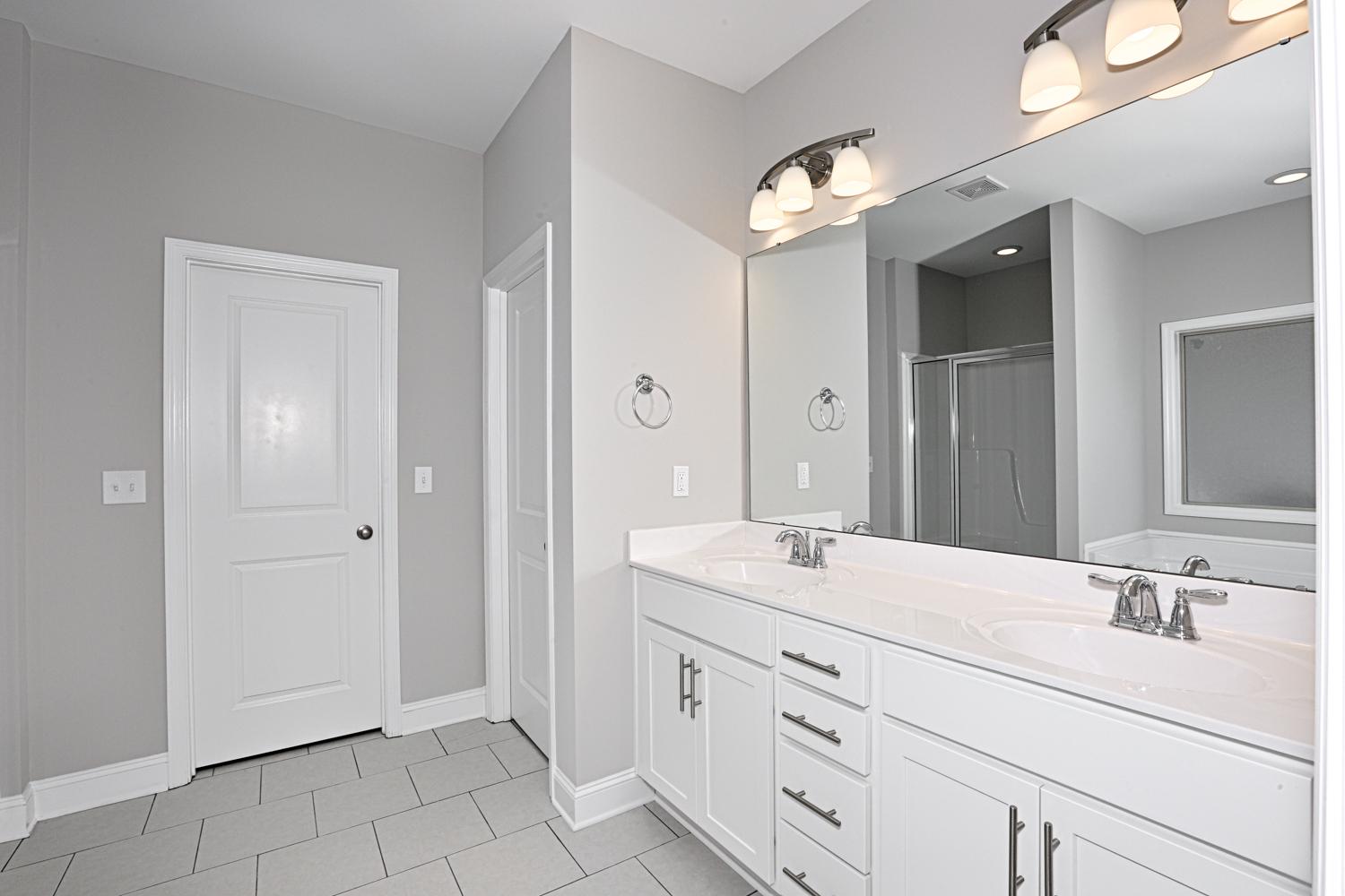 Spacious master bathroom in The Montgomery with double white vanity, gray walls, and glass shower