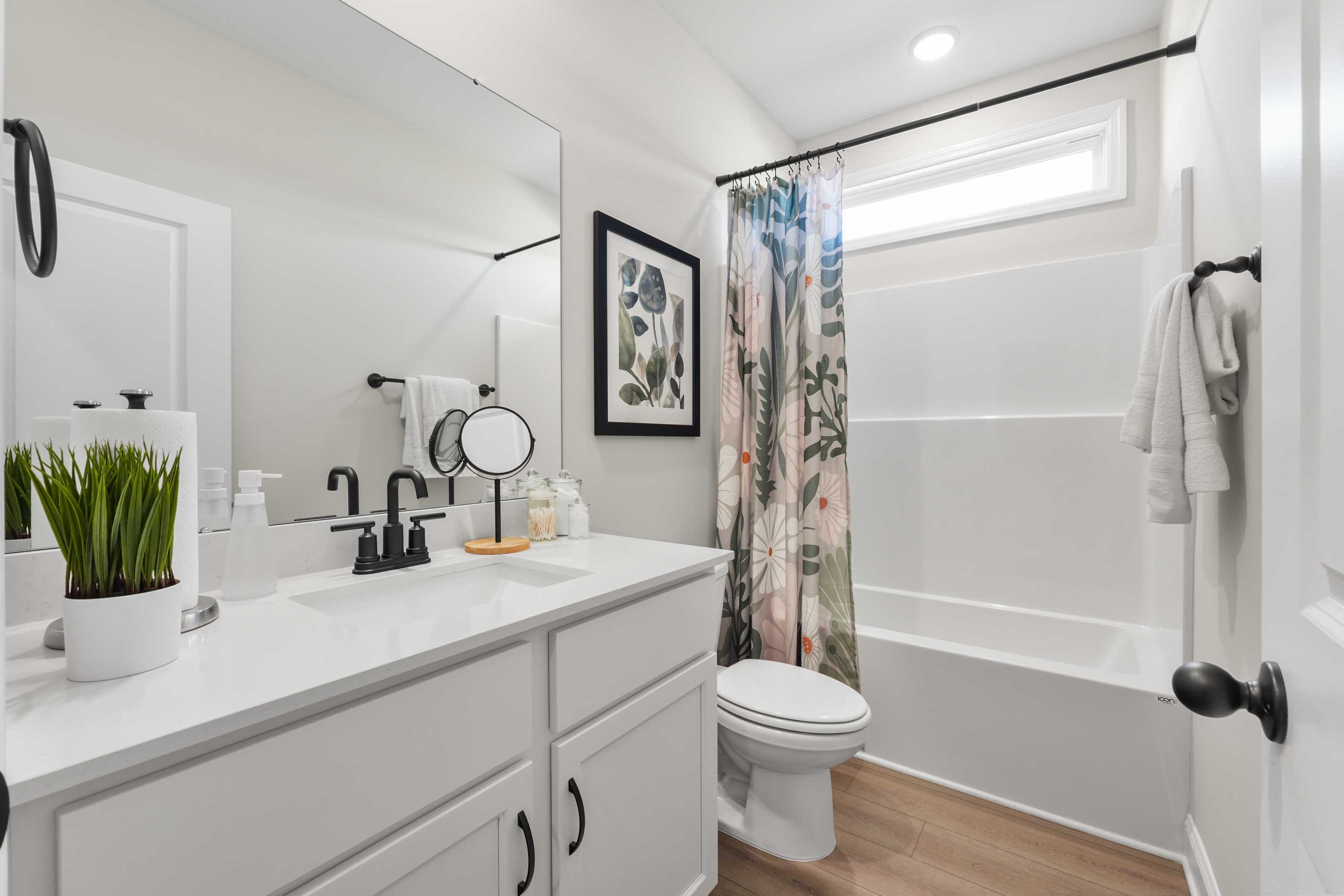 Modern bathroom at Ramsay Cove in Owens Cross Roads AL with white vanity, soaking tub, floral curtains, and potted plant
