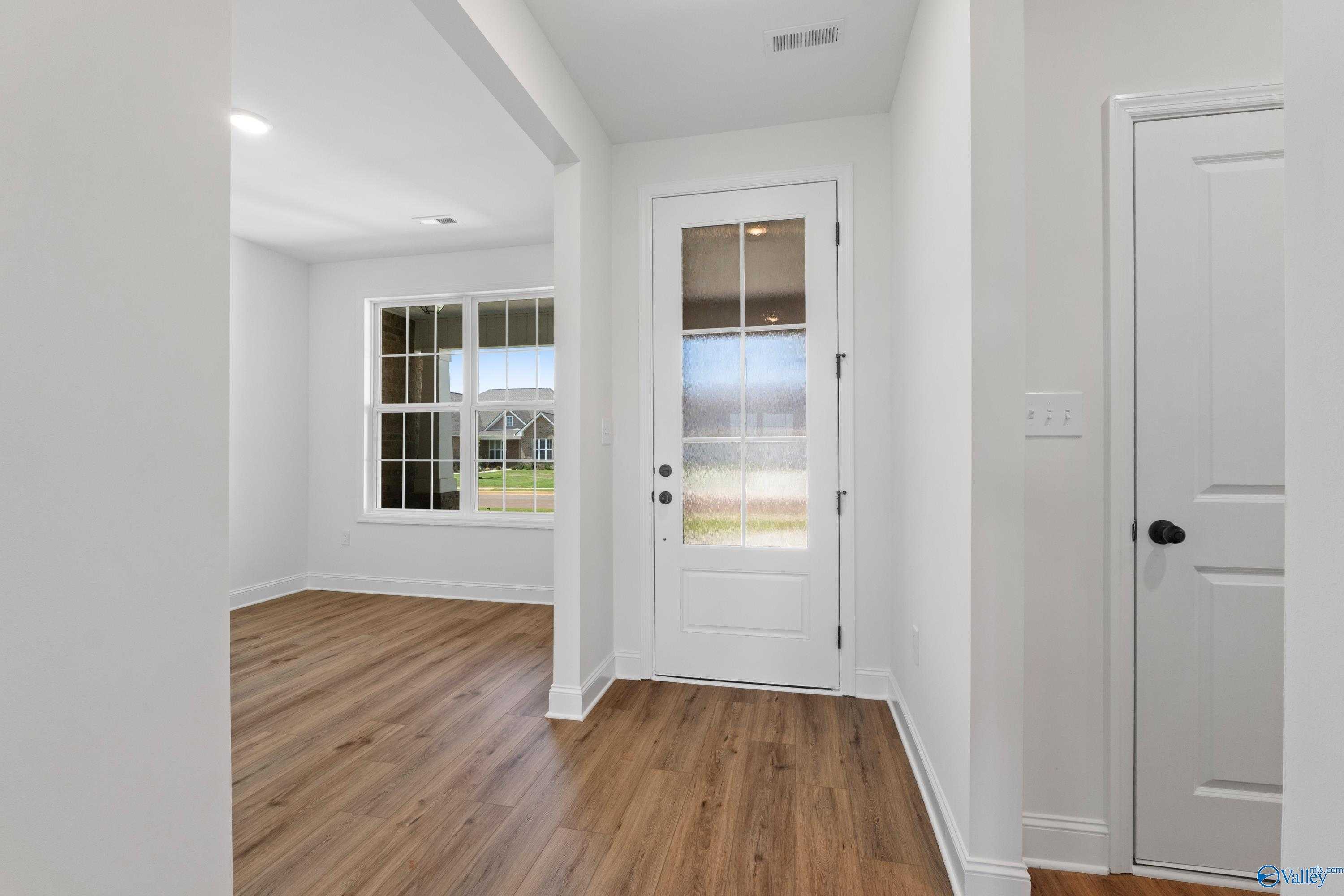 Bright entryway with glass-paneled door, large windows, and hardwood floors in Davidson Homes The Rockford B, Toney, Alabama