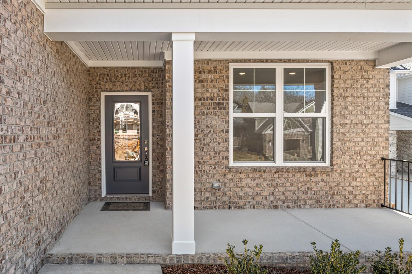 Inviting brick front porch with white columns, gray glass door, and large windows on 2-story Davidson Homes The Ash A in Gallatin, Tennessee
