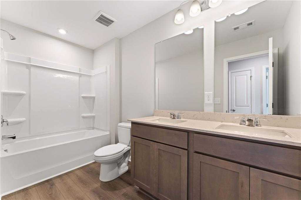 Modern guest bathroom with double shaker vanity, white tub, glass shower, and wood-look flooring in Davidson Homes The Monroe A, Emerson, GA